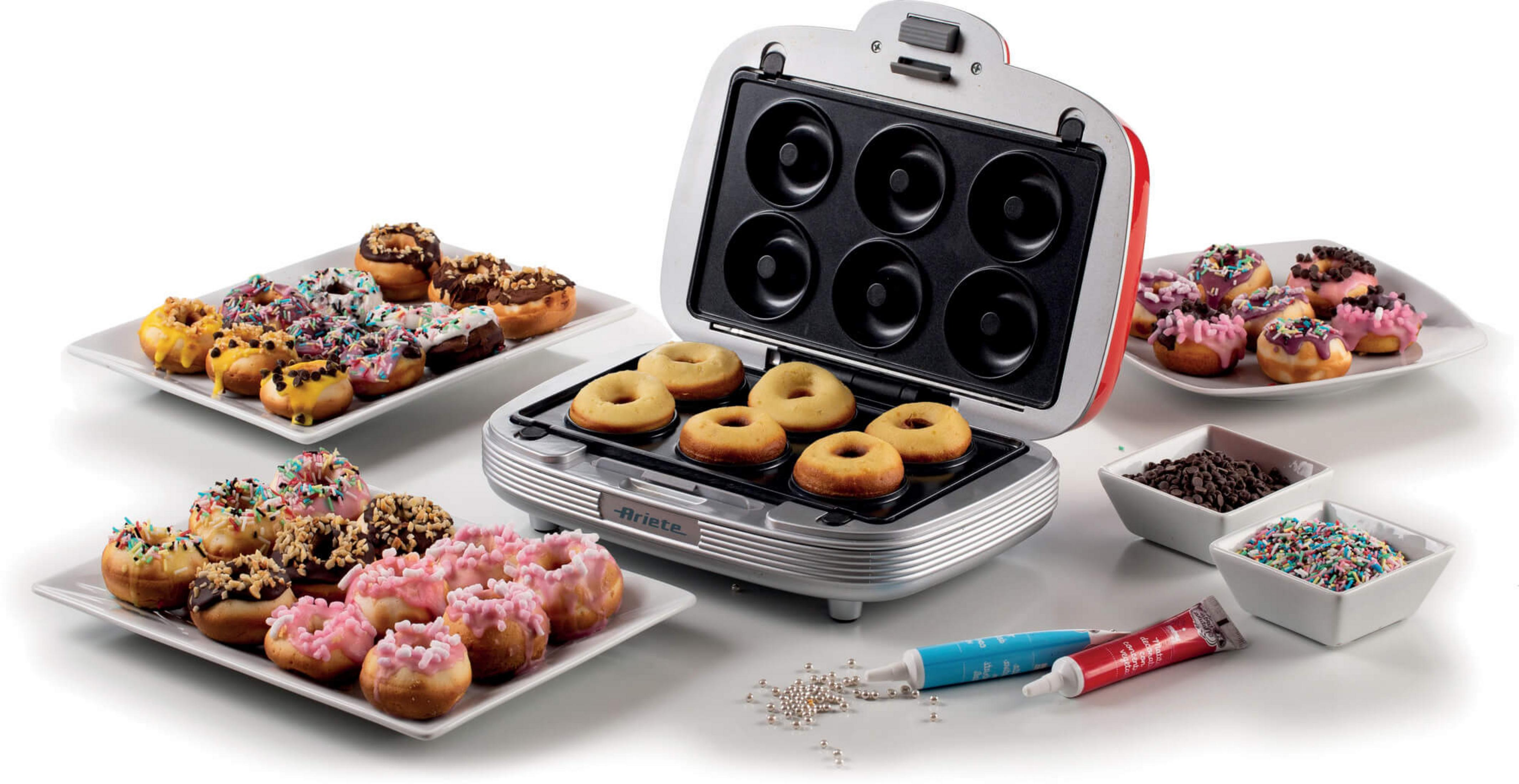 A donut maker with open lid, filled with donuts. Beside it, plates with colorful donuts.
