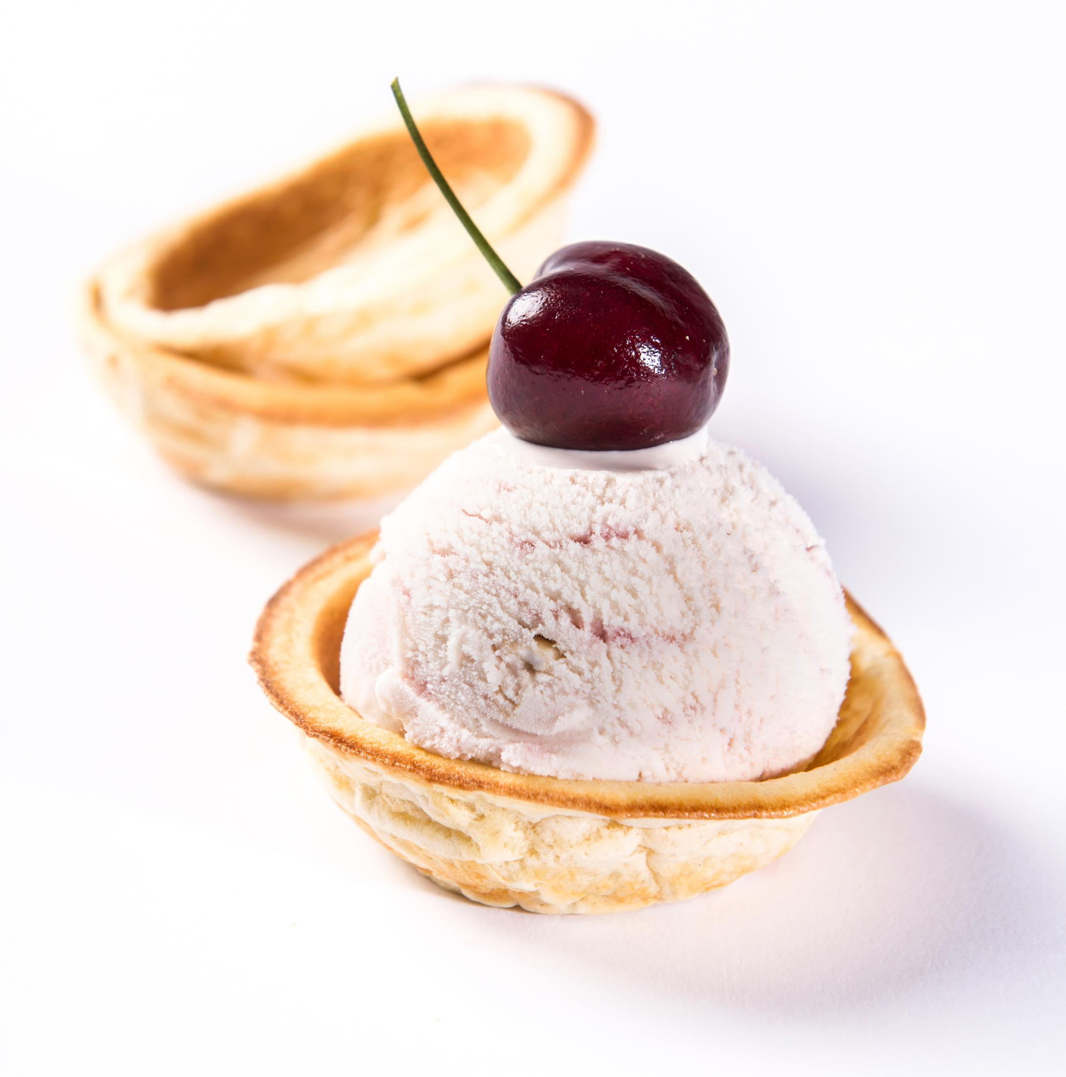 Un cono di gelato in una coppetta di pastella con una ciliegia sopra. Coppette vuote.