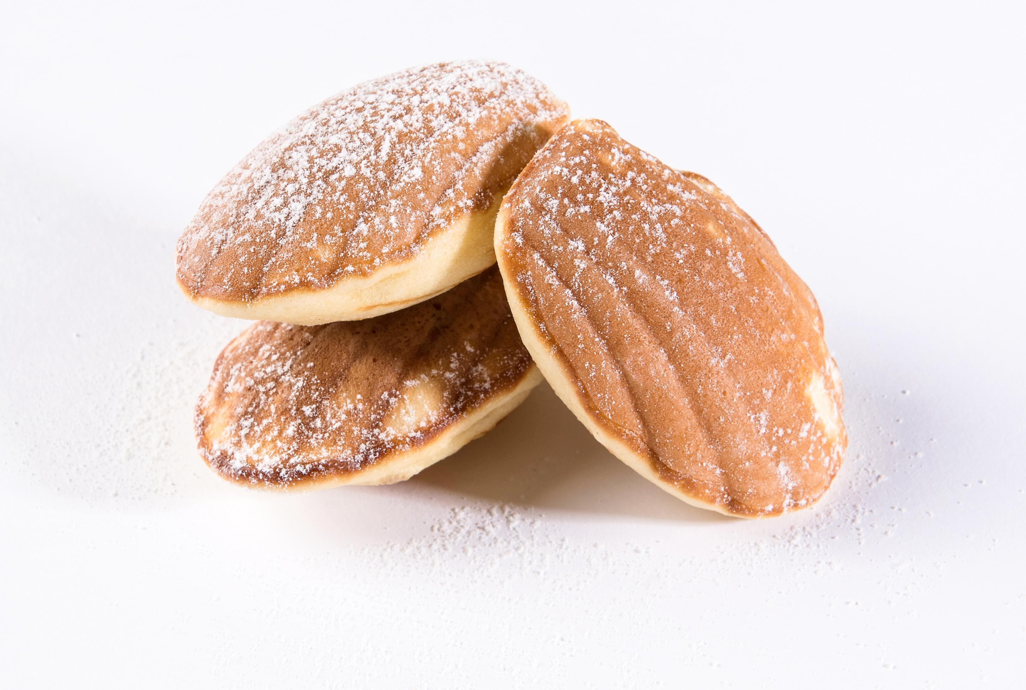 Tre madeleine cosparse di zucchero a velo su sfondo bianco.