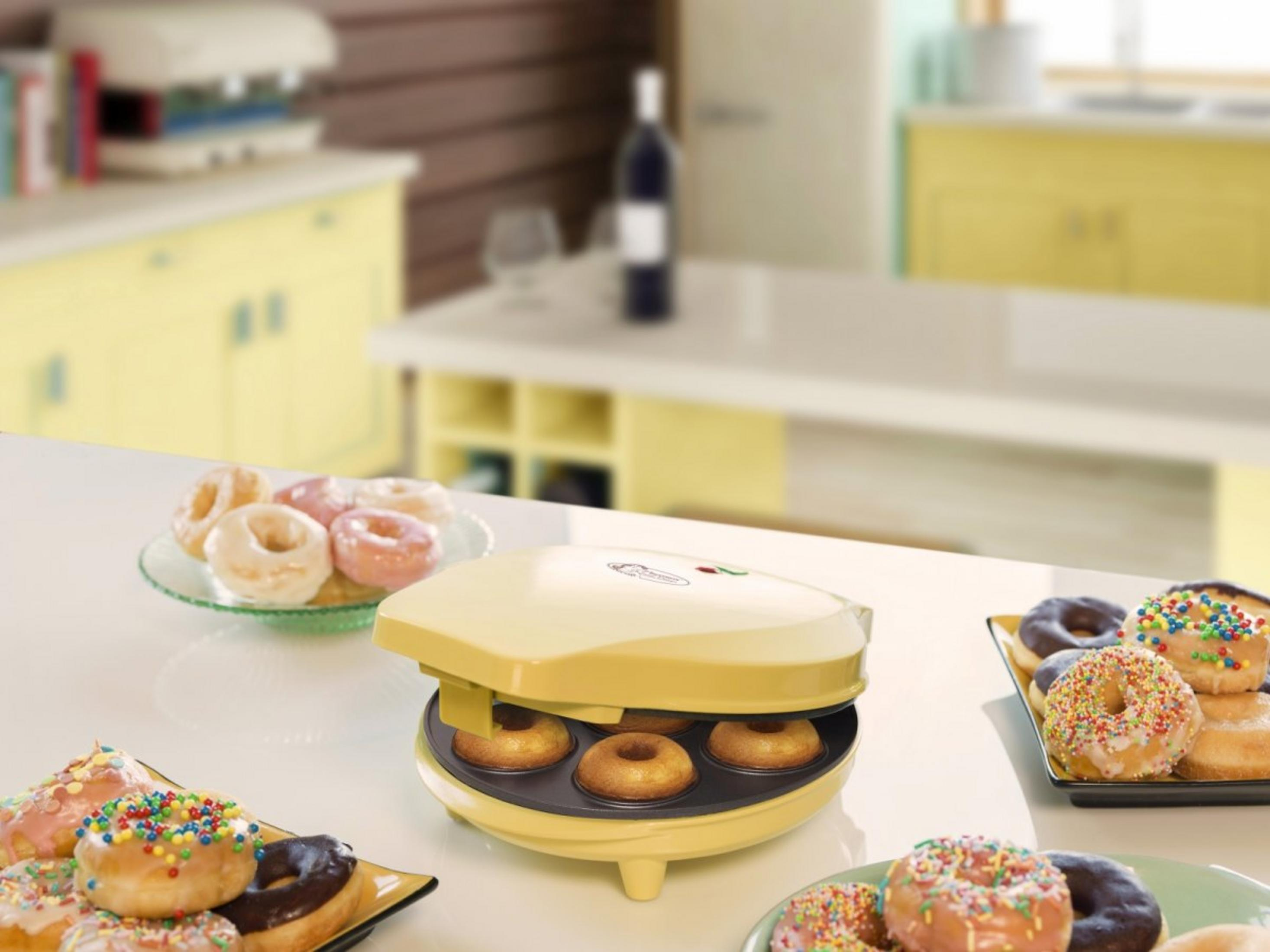 Ein gelber Donut-Maker mit vier Donuts, daneben Platten mit fertigen Donuts.