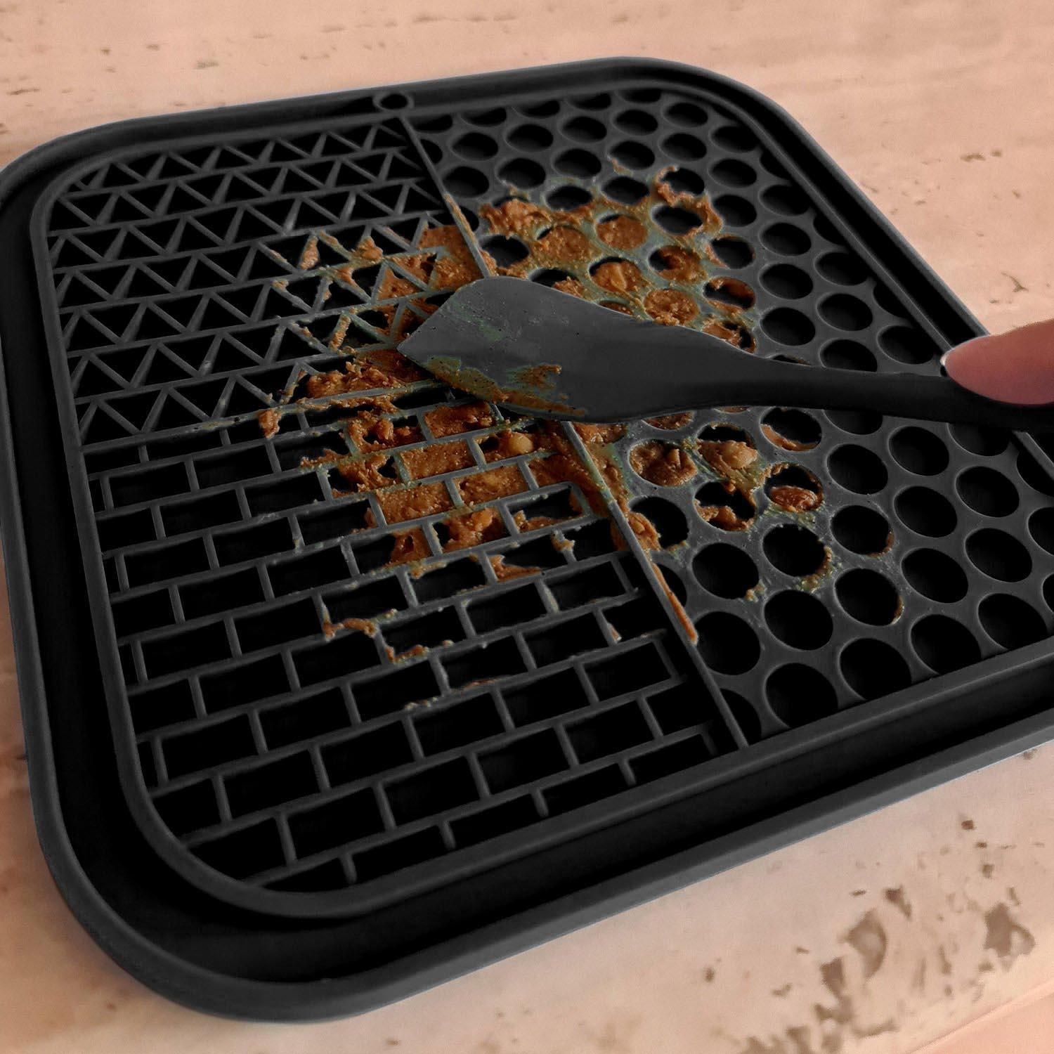 Una rejilla negra con residuos de comida se limpia con una espátula.