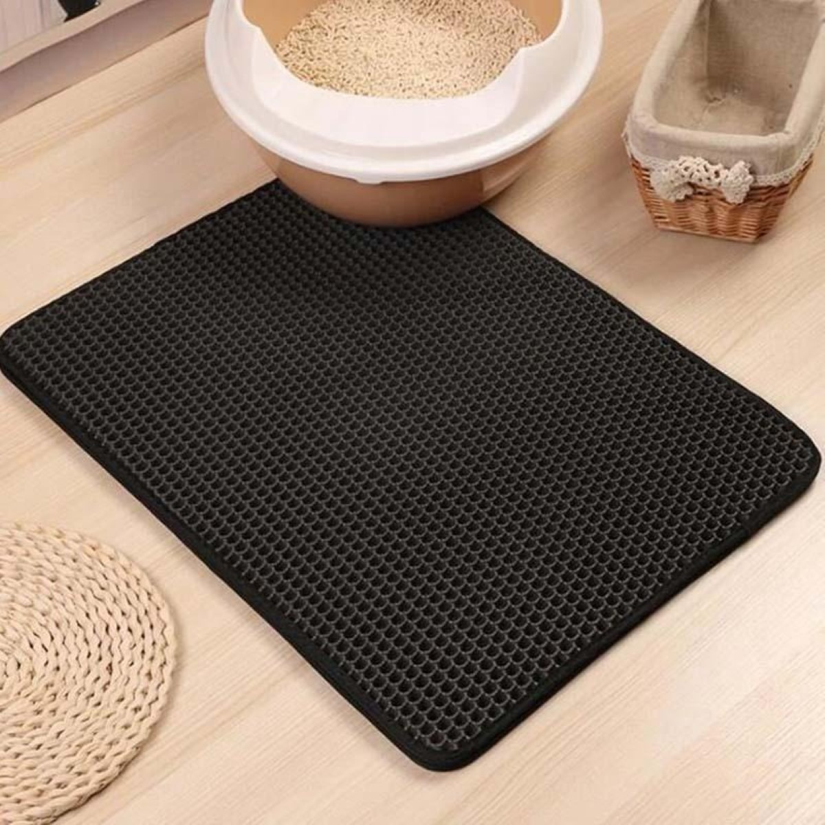 Alfombrilla negra para arena de gato con panal sobre suelo de madera.