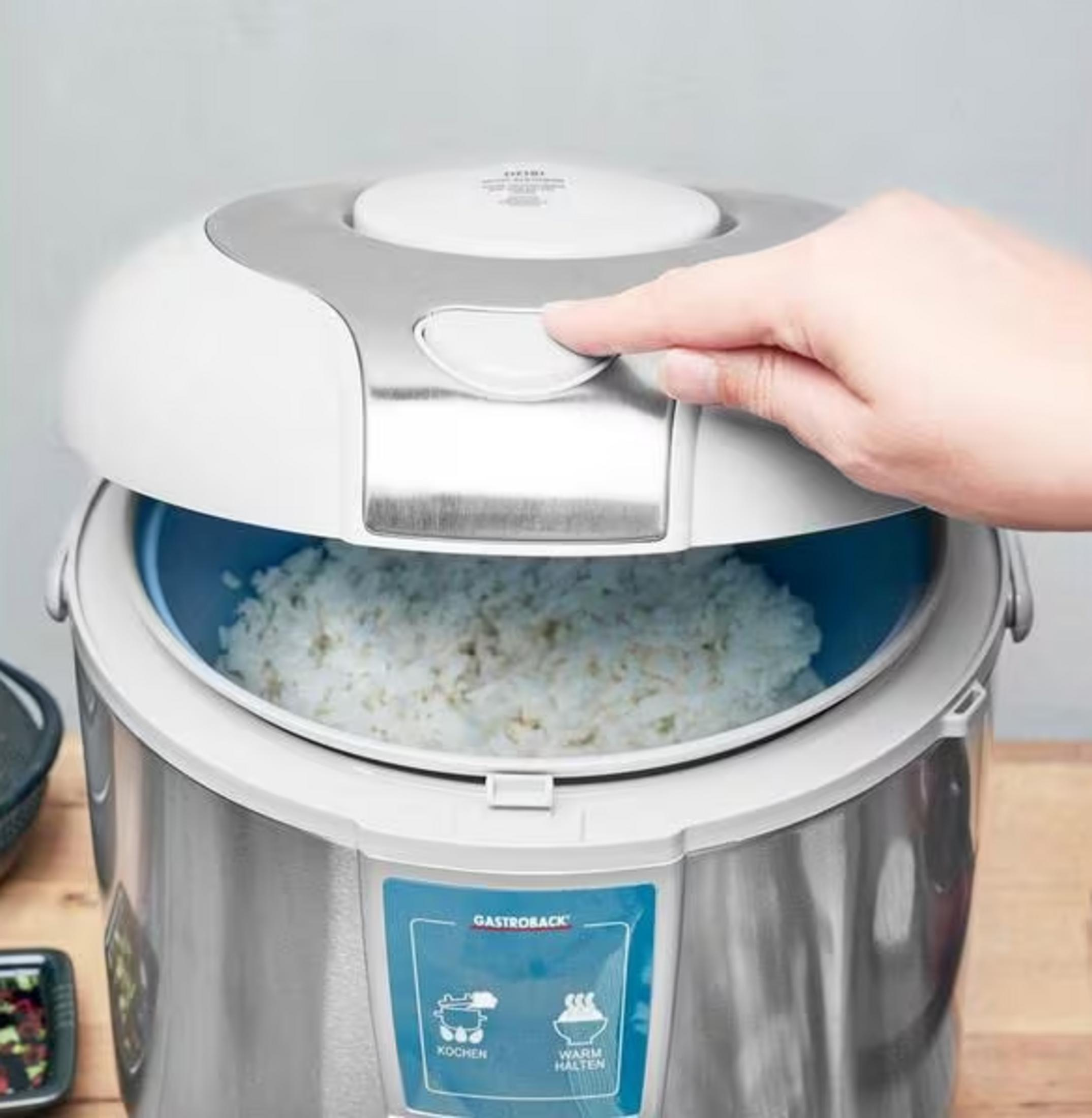 Una mano apre il coperchio di una pentola per riso con riso cotto all'interno.