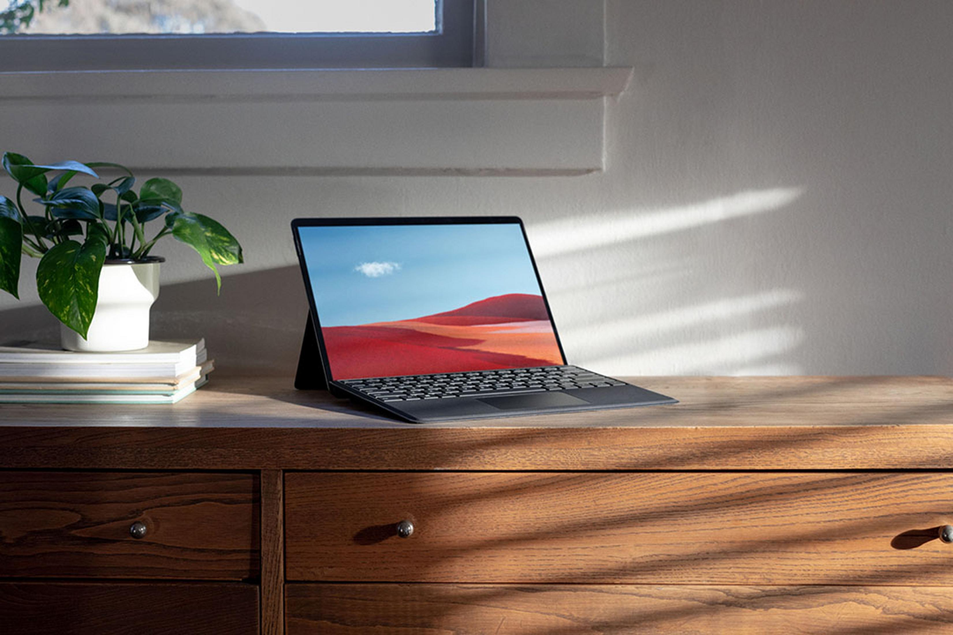 Un laptop con tastiera nera su un mobile di legno. Una pianta a sinistra.