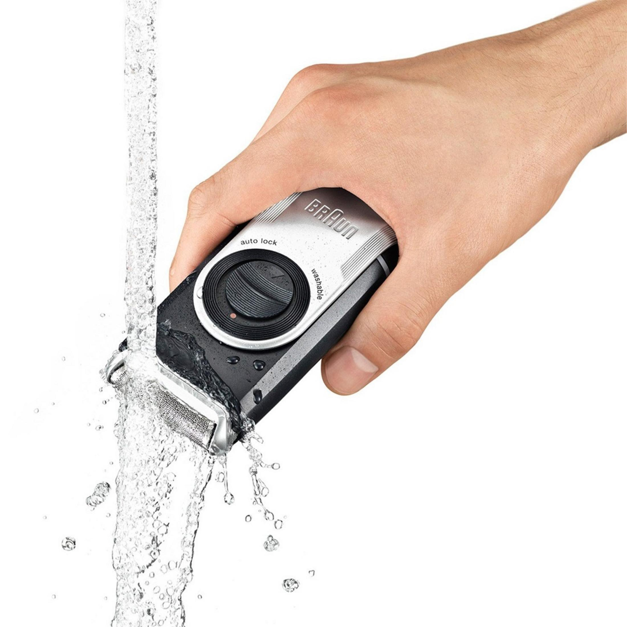 Una mano tiene un rasoio Braun nero sotto l'acqua corrente.