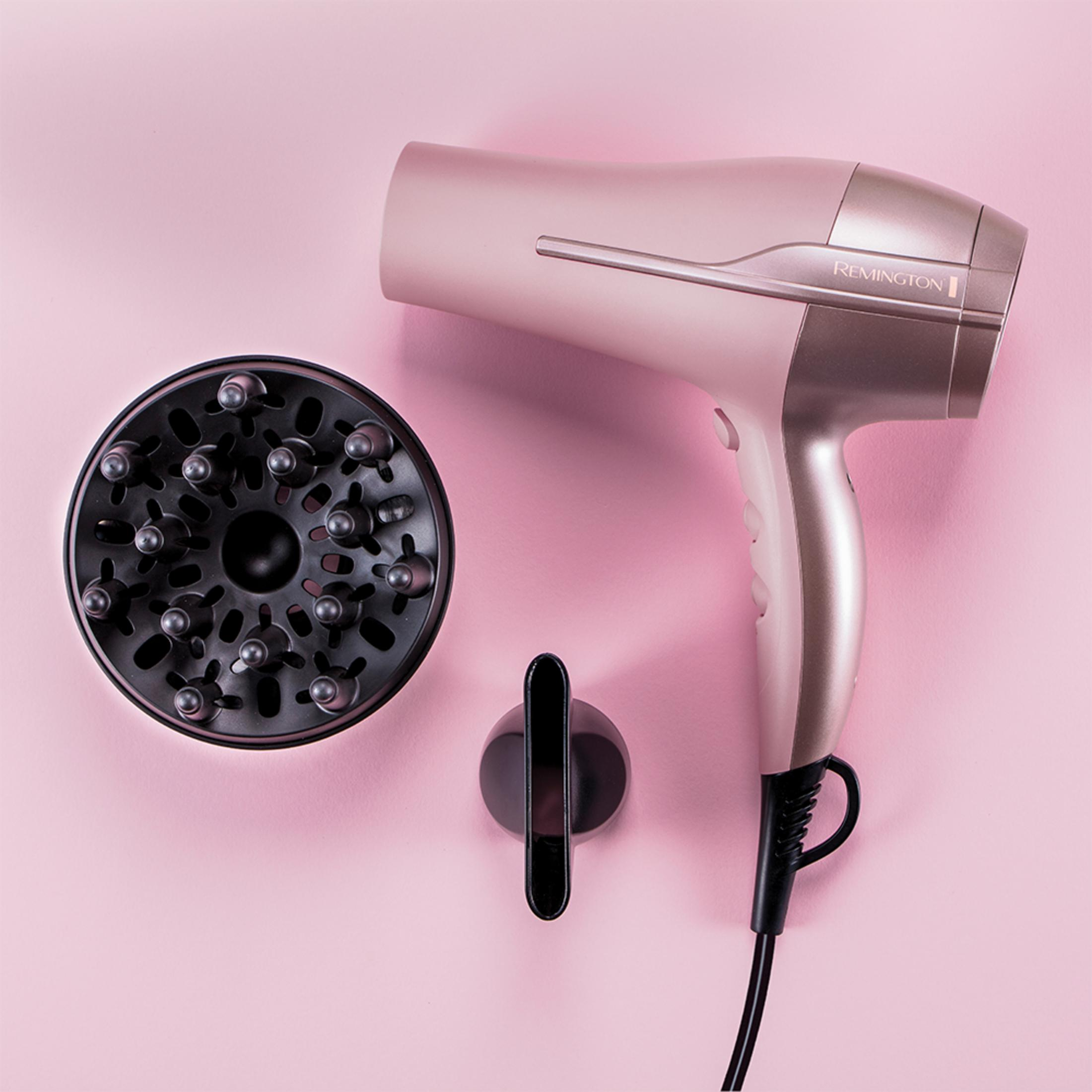 Een roségouden Remington föhn met diffuser en concentratormondstuk op roze achtergrond.