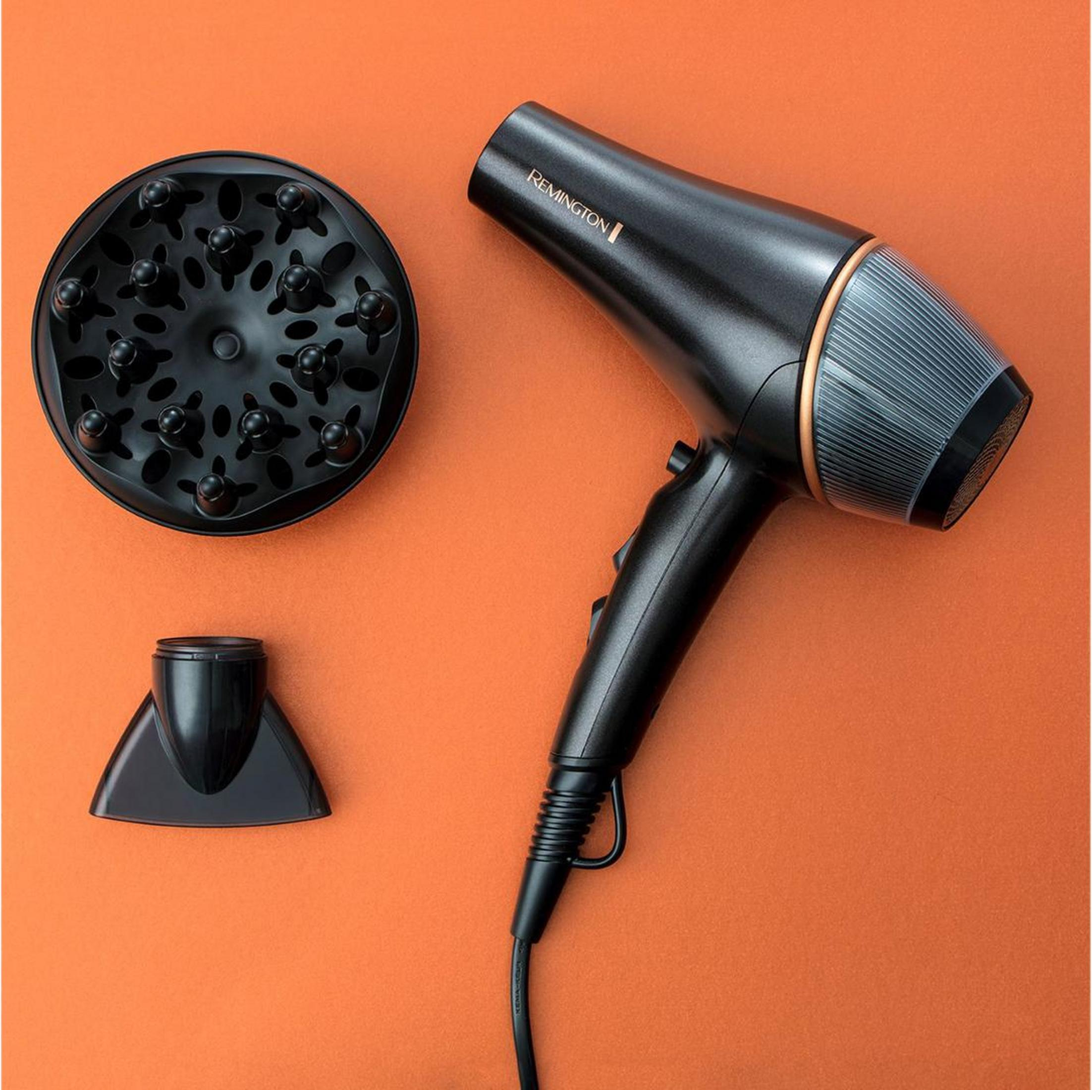 Un asciugacapelli Remington nero con diffusore e ugello concentratore su sfondo arancione.