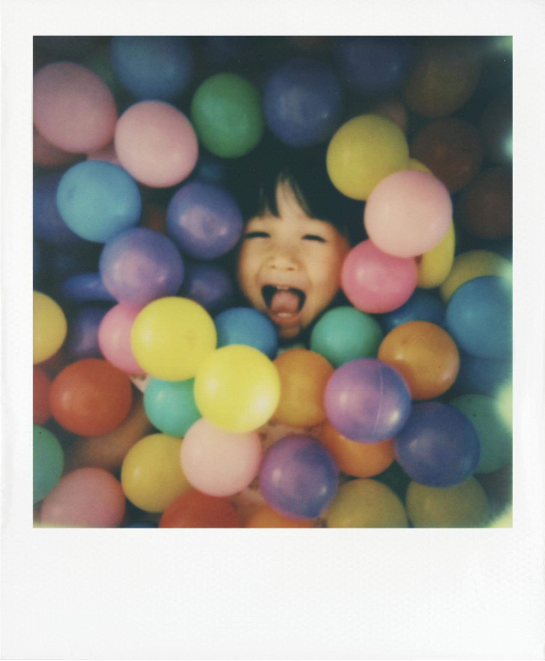 Un niño riendo mete la cabeza entre pelotas de colores.