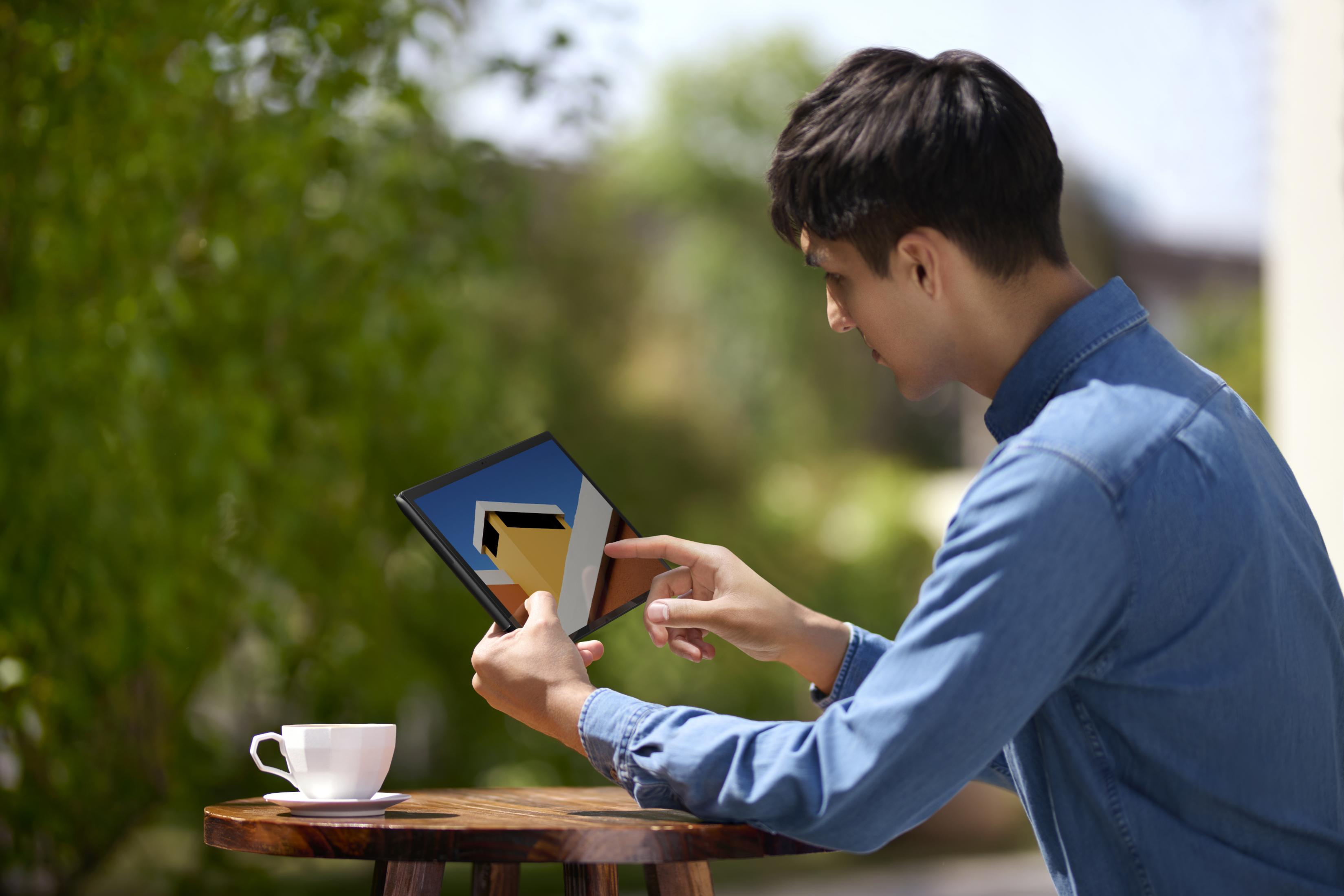Man in spijkerhemd kijkt naar tablet met huismodel. Koffiekopje ernaast.