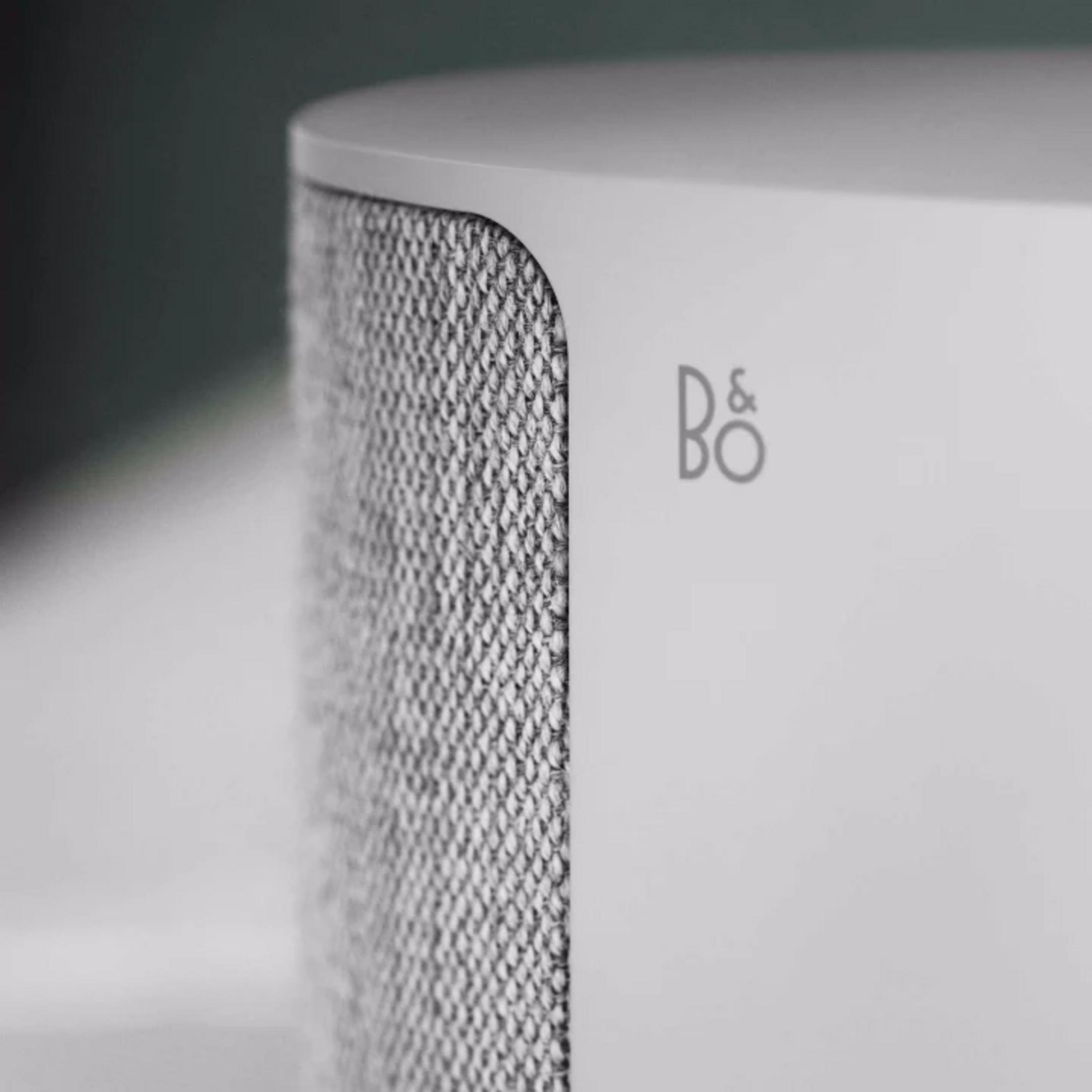 Ein weißer Lautsprecher mit silbernem Stoff und dem B&O-Logo.