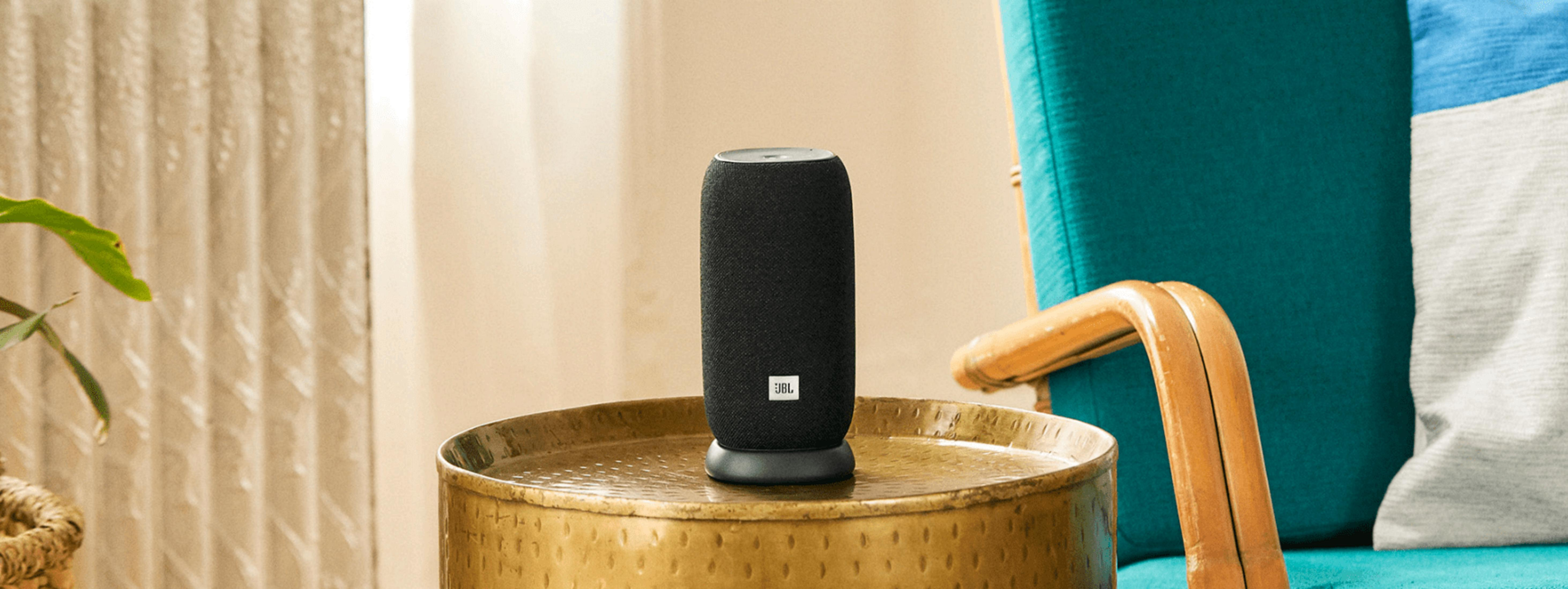 Un altavoz JBL negro se sienta en una mesa dorada junto a una silla turquesa.