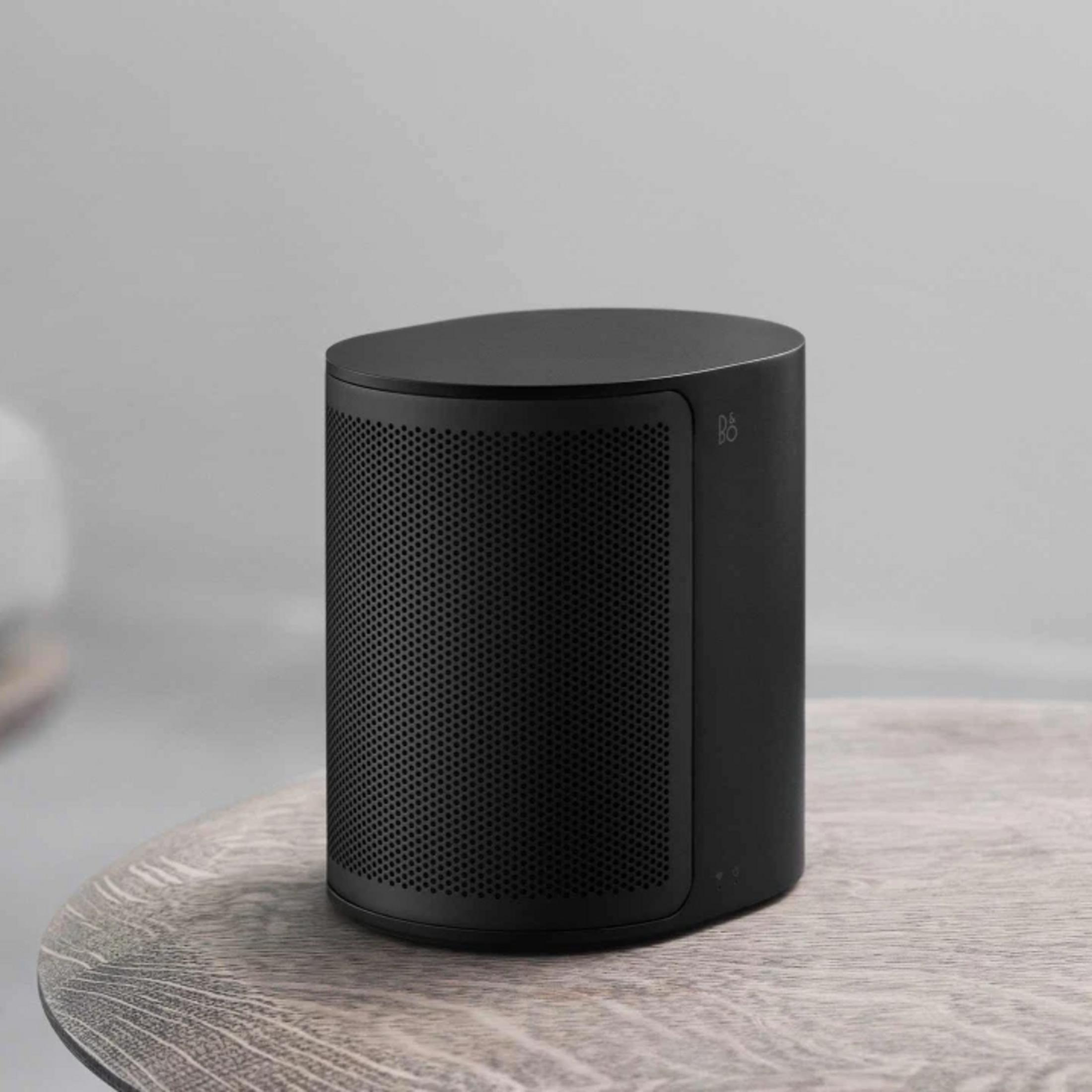 Un altavoz cilíndrico negro con patrón perforado se sienta sobre una mesa de madera.