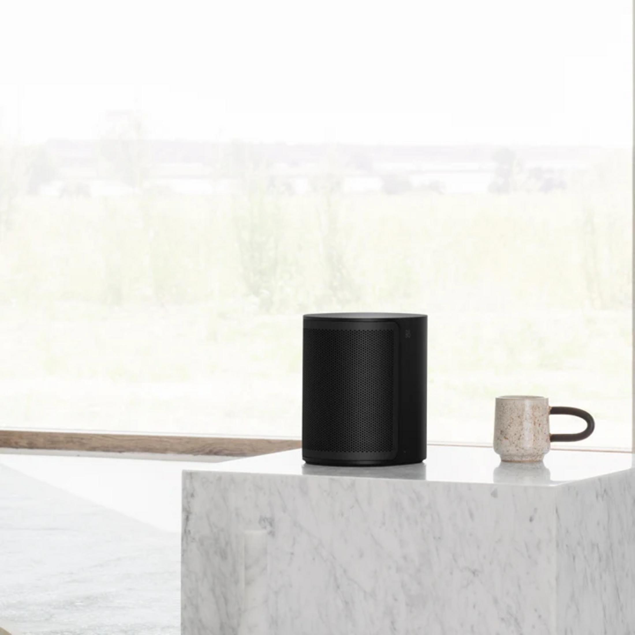 Un altavoz negro y una taza estampada sobre una mesa de mármol.