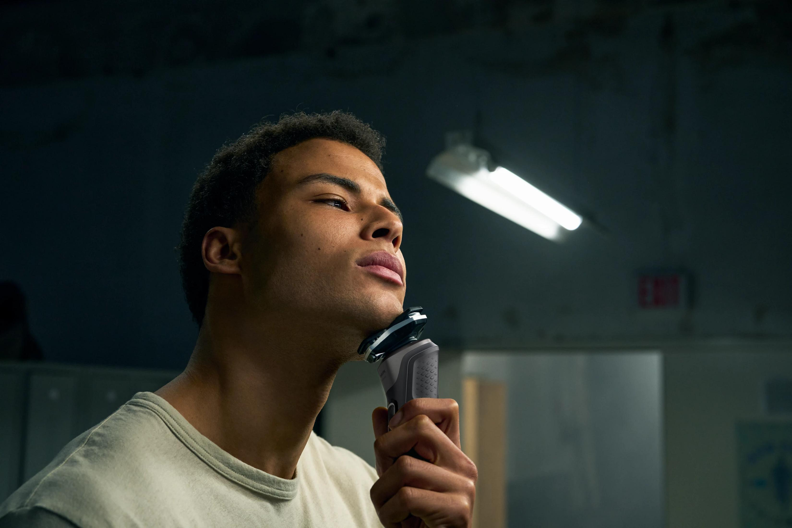 Mężczyzna goli twarz golarką elektryczną. Ciemne tło z oświetleniem.
