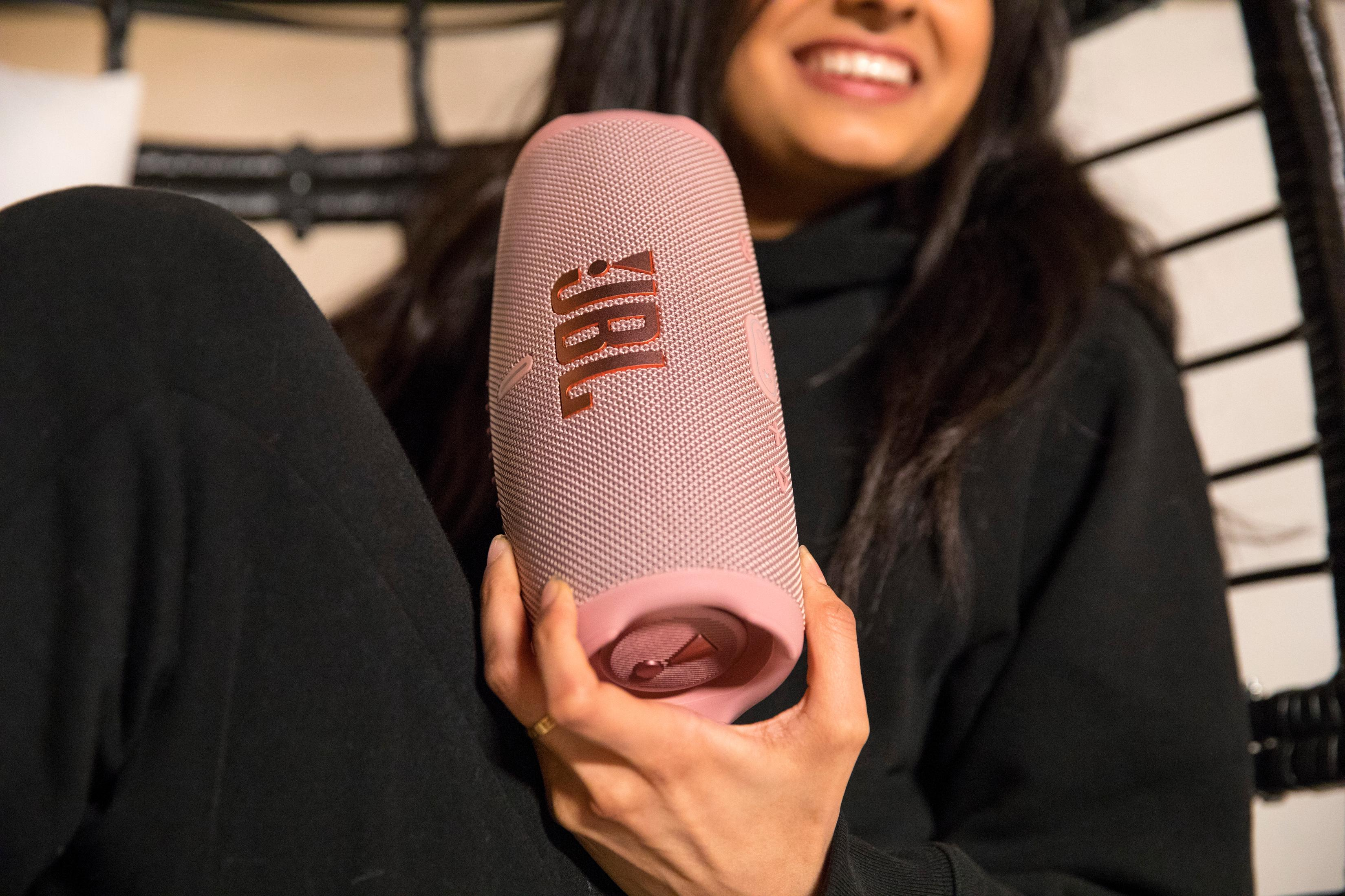 Kobieta trzyma różowy głośnik JBL z logo JBL.