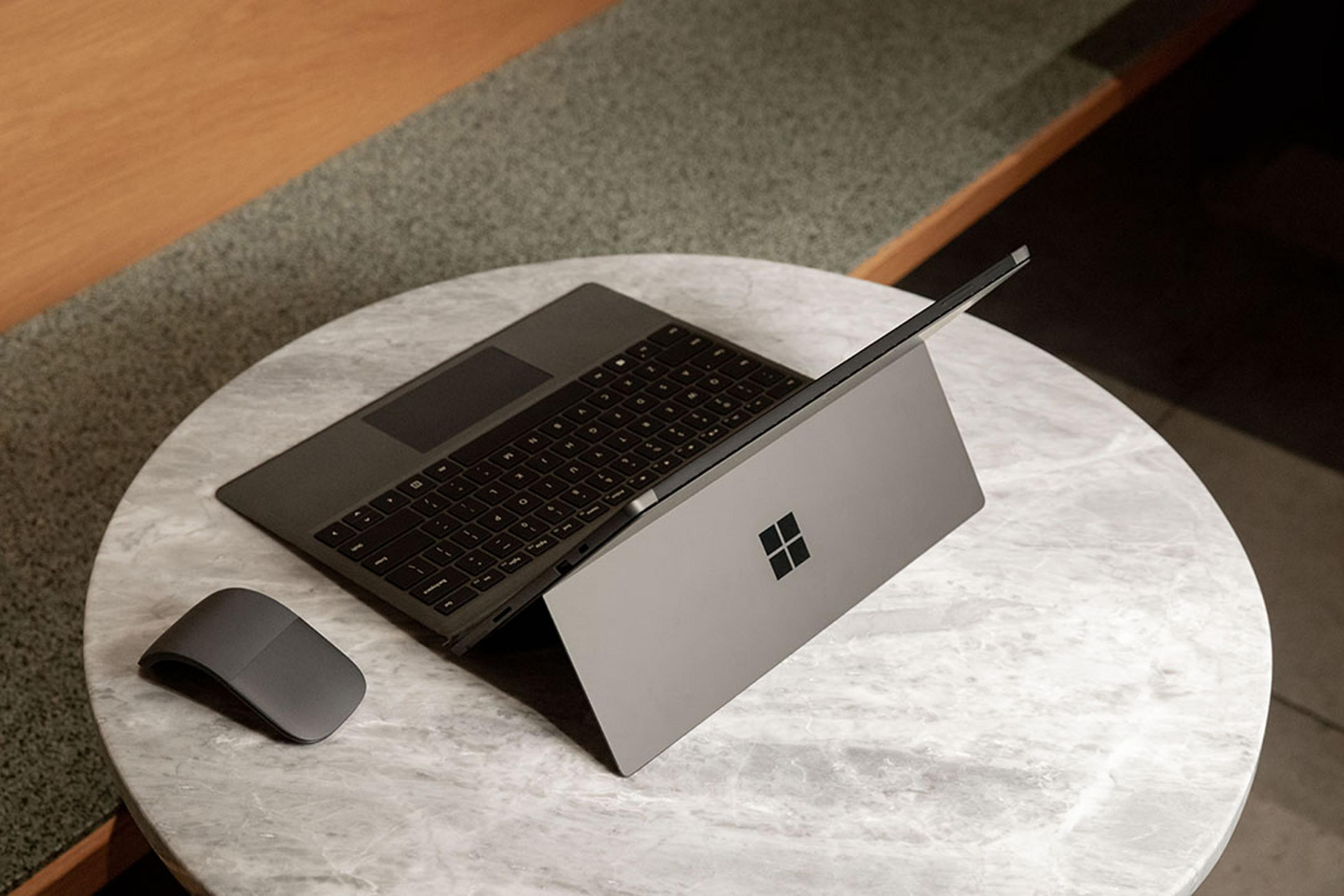 Ein graues Surface Laptop Studio mit Maus auf einem Marmortisch.