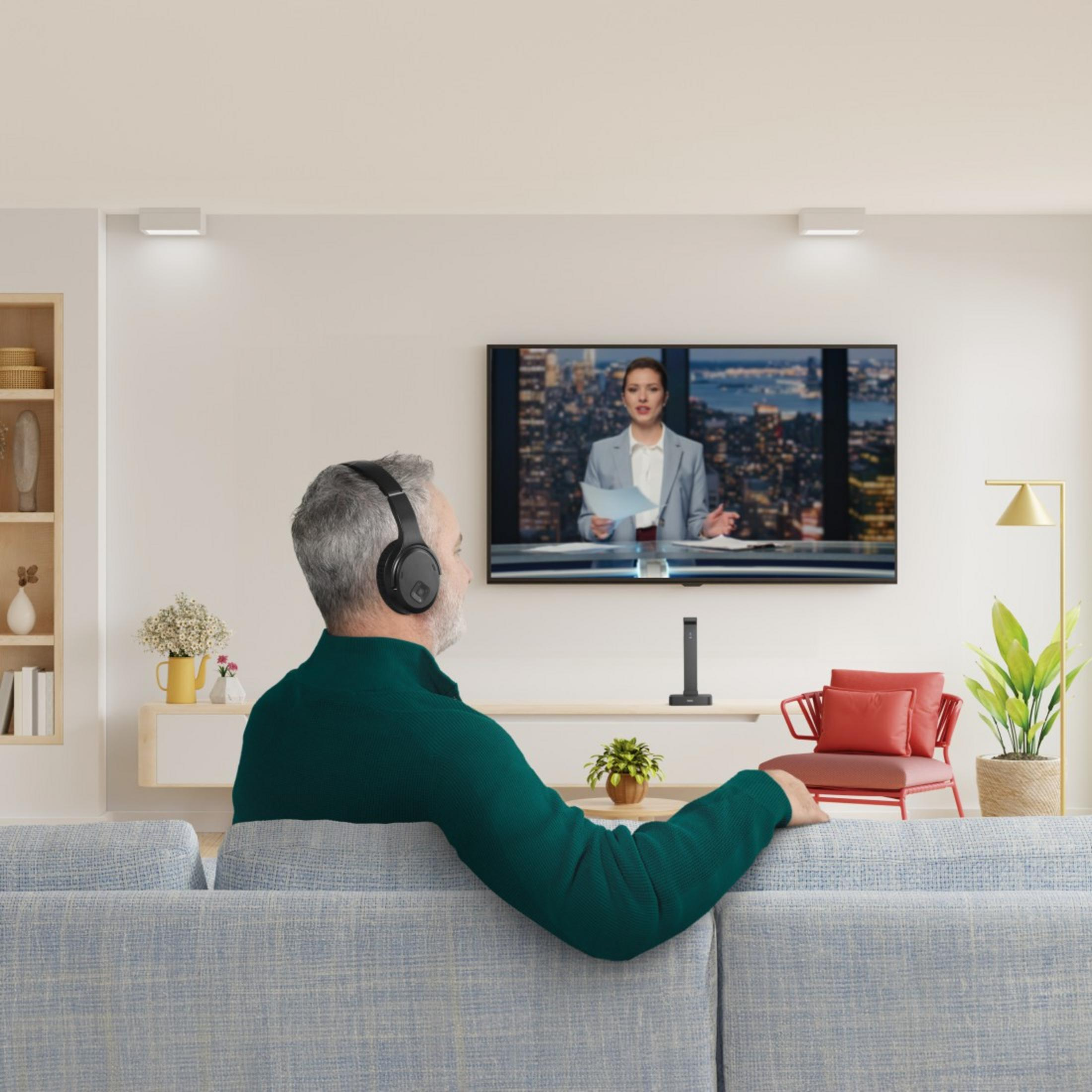 Mann mit Kopfhörern sitzt auf Sofa und schaut Nachrichtensprecherin im TV.