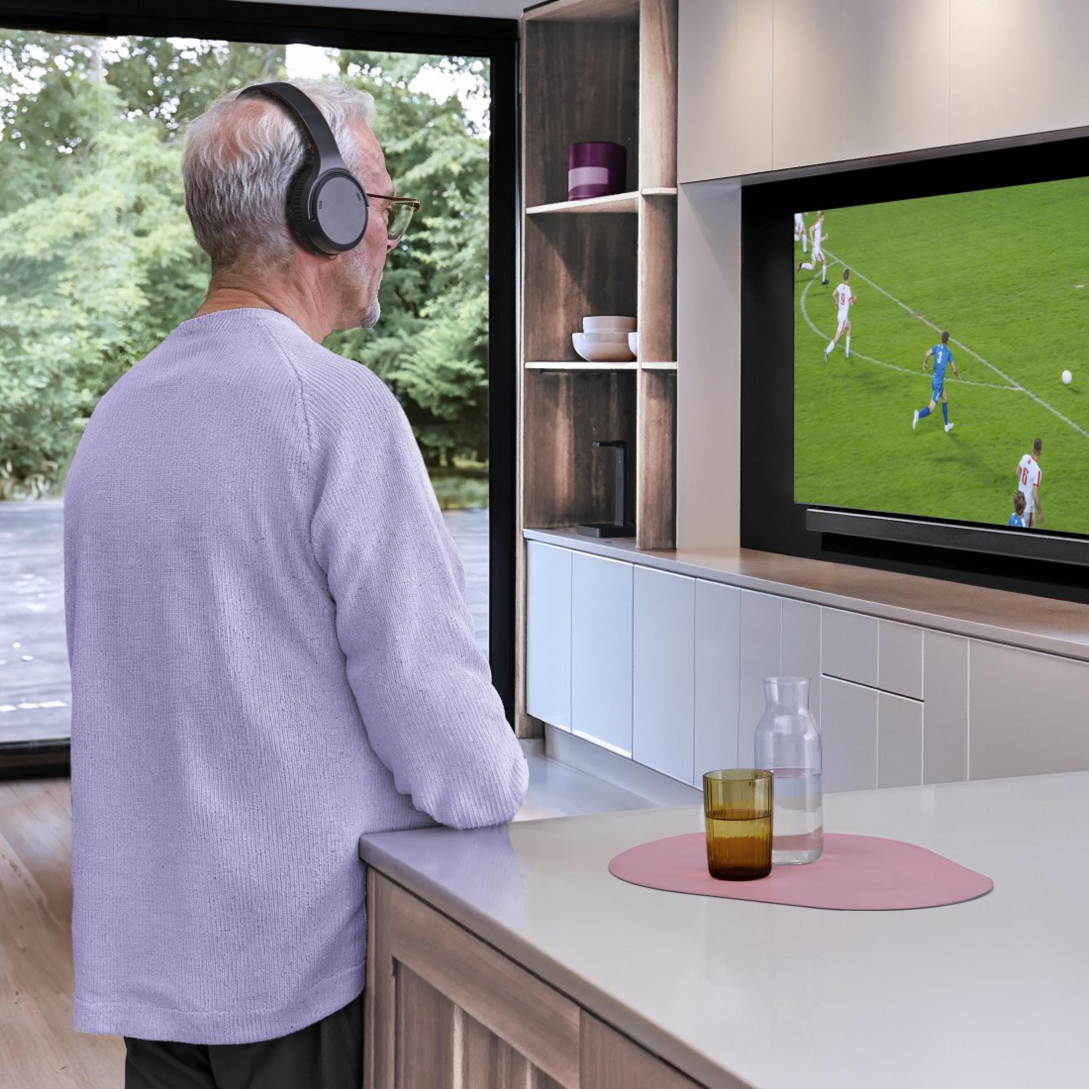 Ein älterer Mann mit Kopfhörern schaut Fußball im Fernsehen.