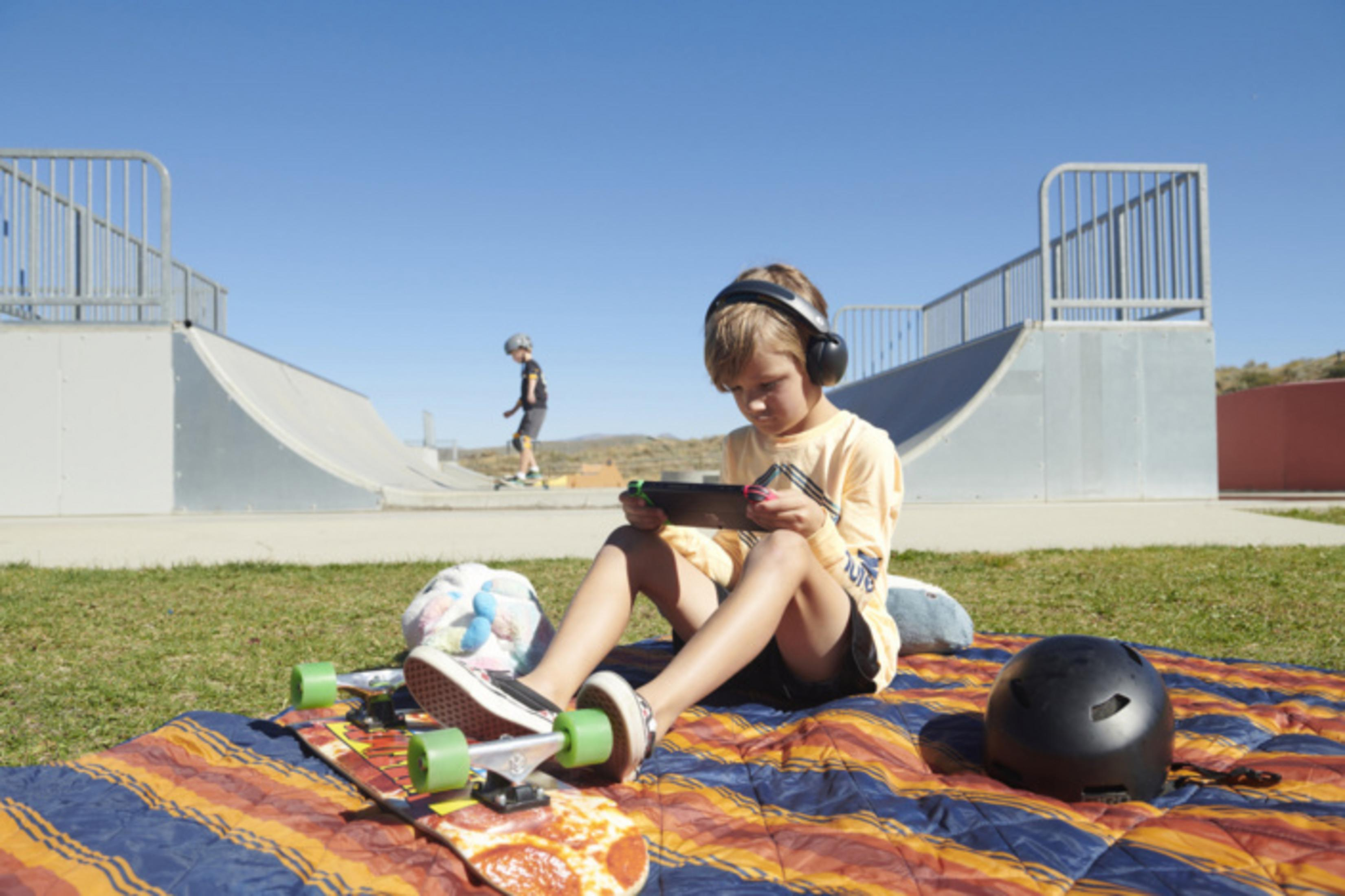 Chłopiec w słuchawkach gra na macie deskorolkowej na zewnątrz.