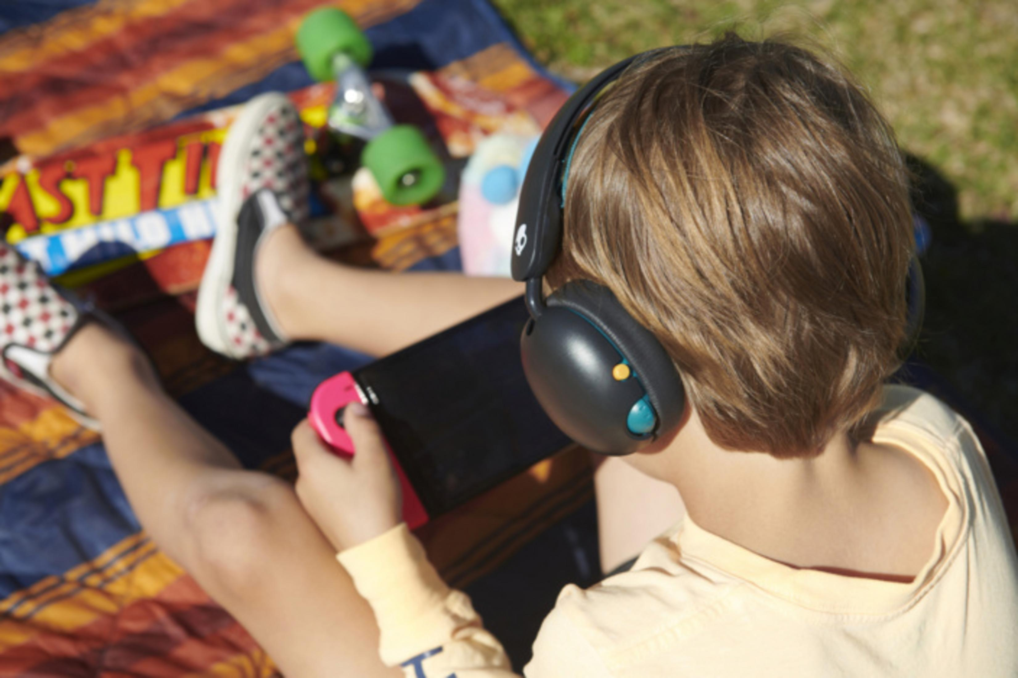 Dziecko w słuchawkach gra na Nintendo Switch na zewnątrz na kocu.