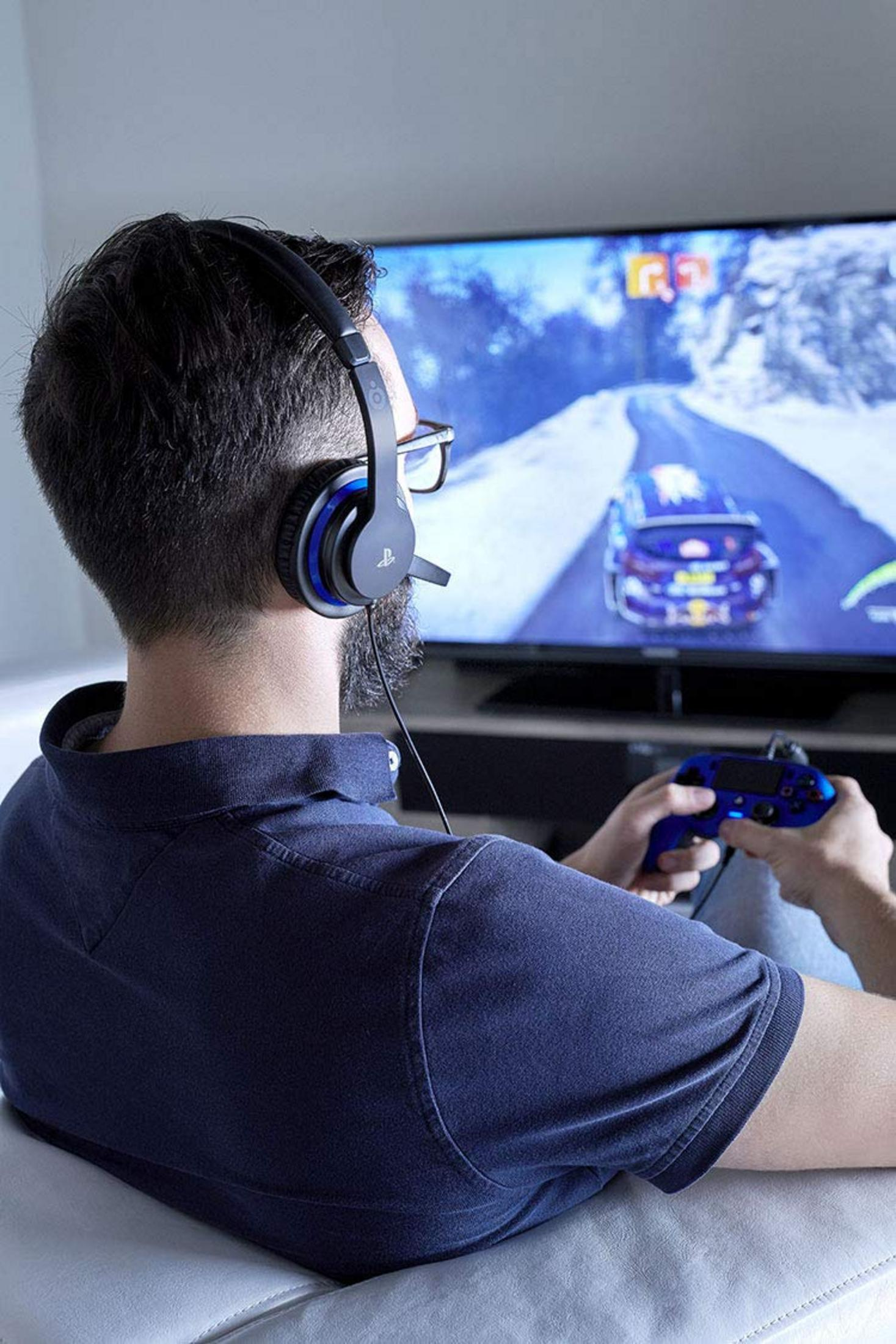 Mann mit Kopfhörern spielt Videospiel auf dem Fernseher und hält einen Controller.