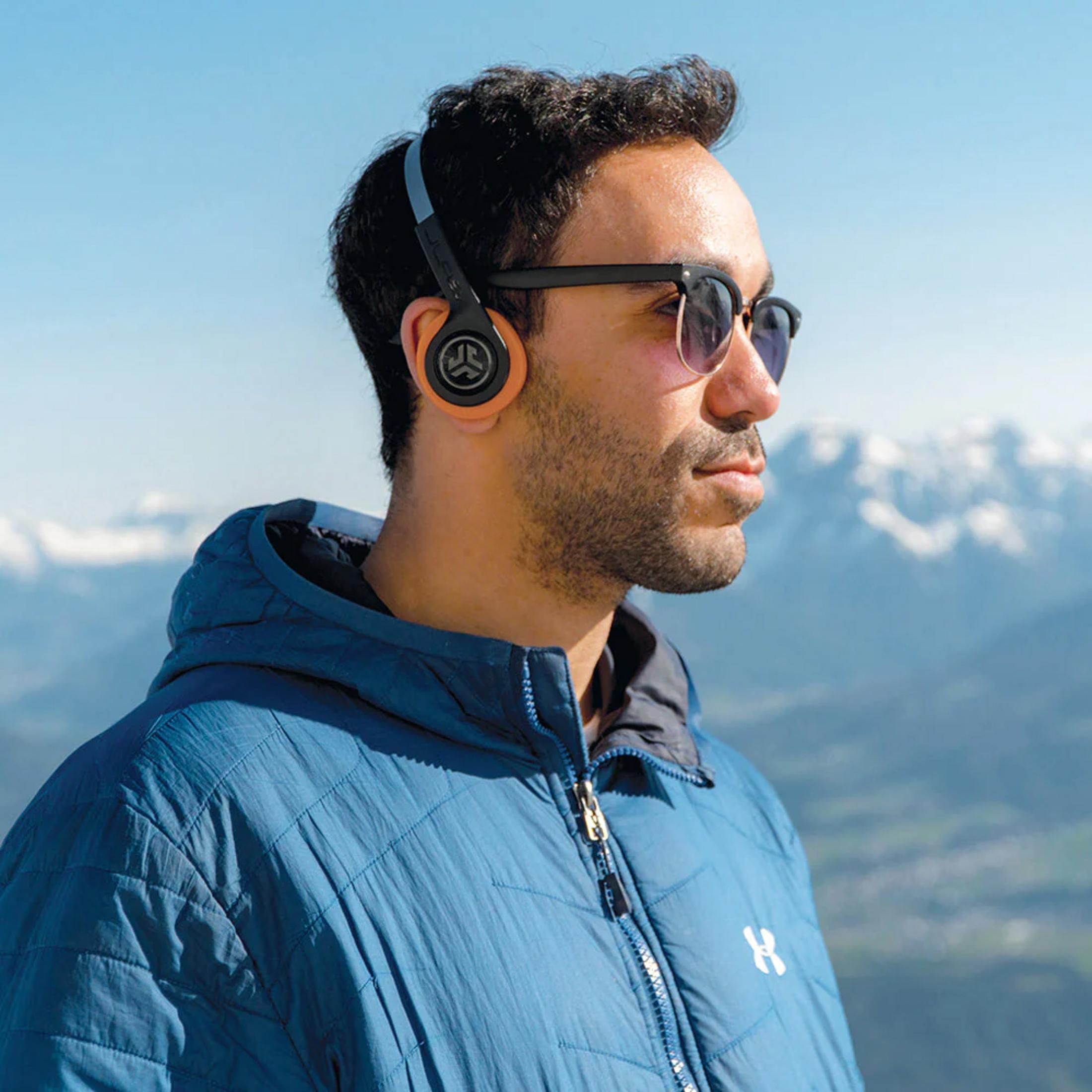 Mann mit Kopfhörern und Sonnenbrille steht vor verschneiten Bergen.