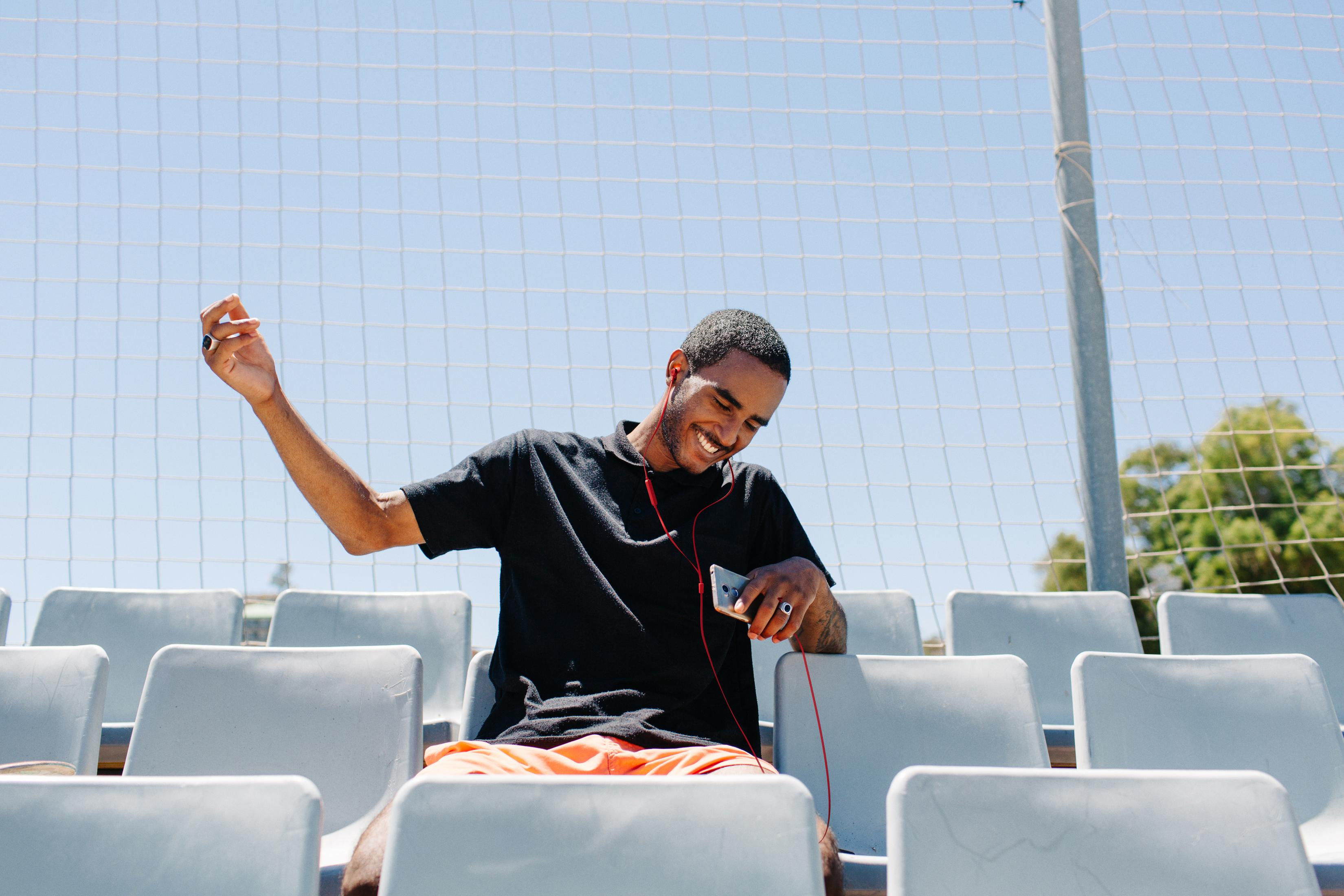 Mężczyzna w czarnym polo siedzi na trybunach, słucha muzyki przez słuchawki.