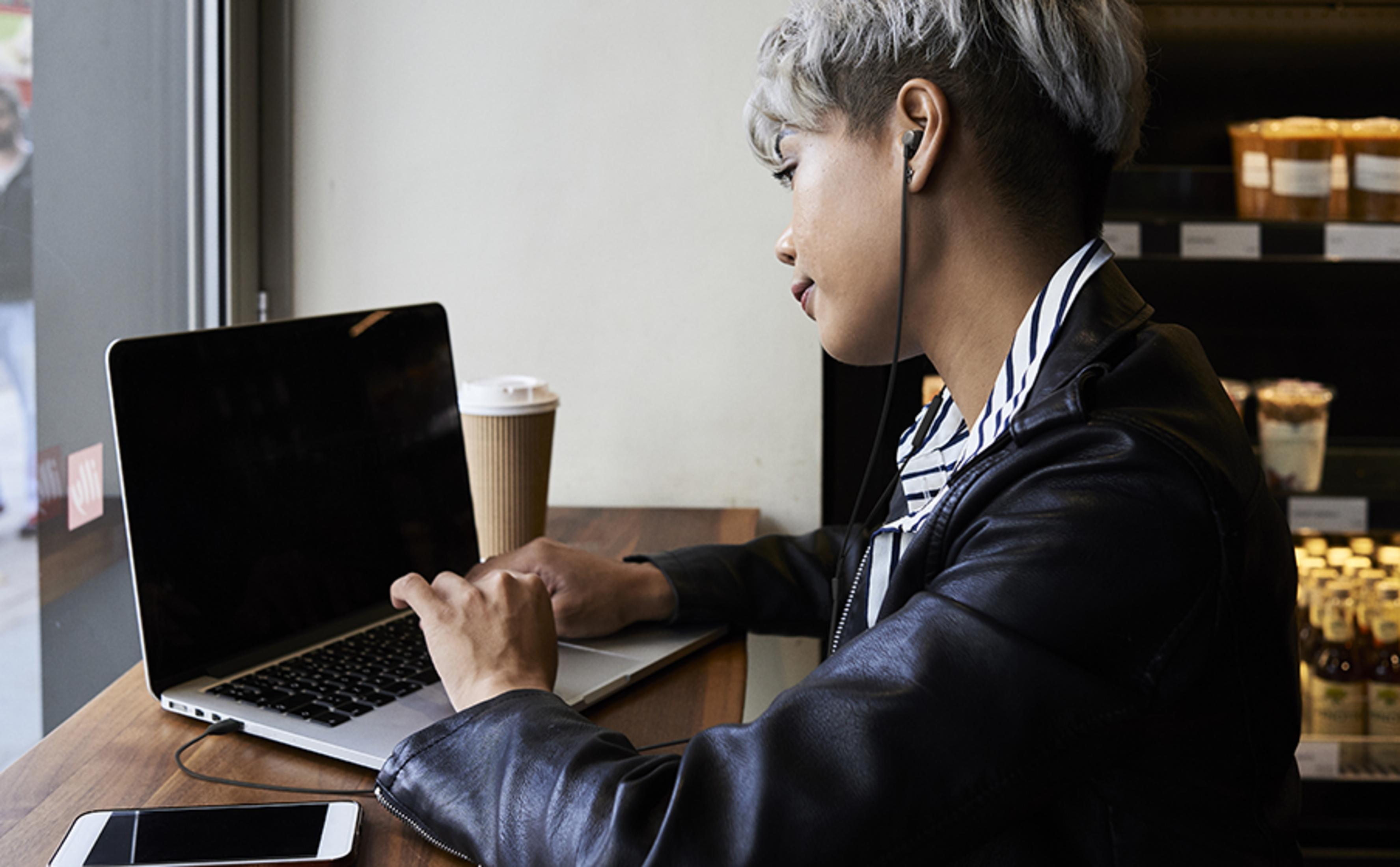 Osoba z krótkimi, siwymi włosami pisze na laptopie w kawiarni.