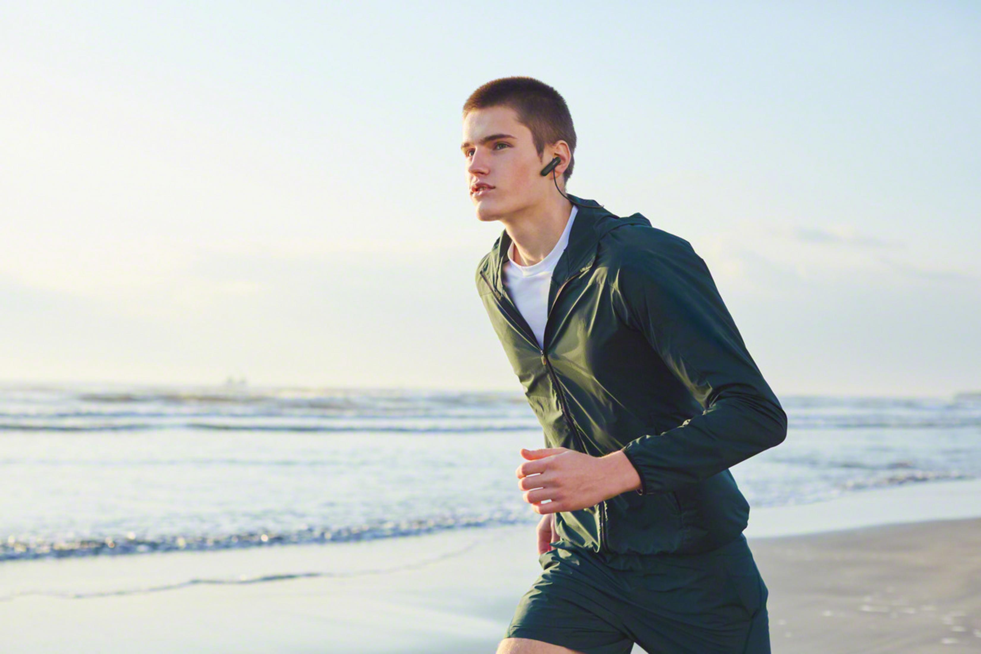 Mężczyzna biegnie po plaży z słuchawkami w uszach.