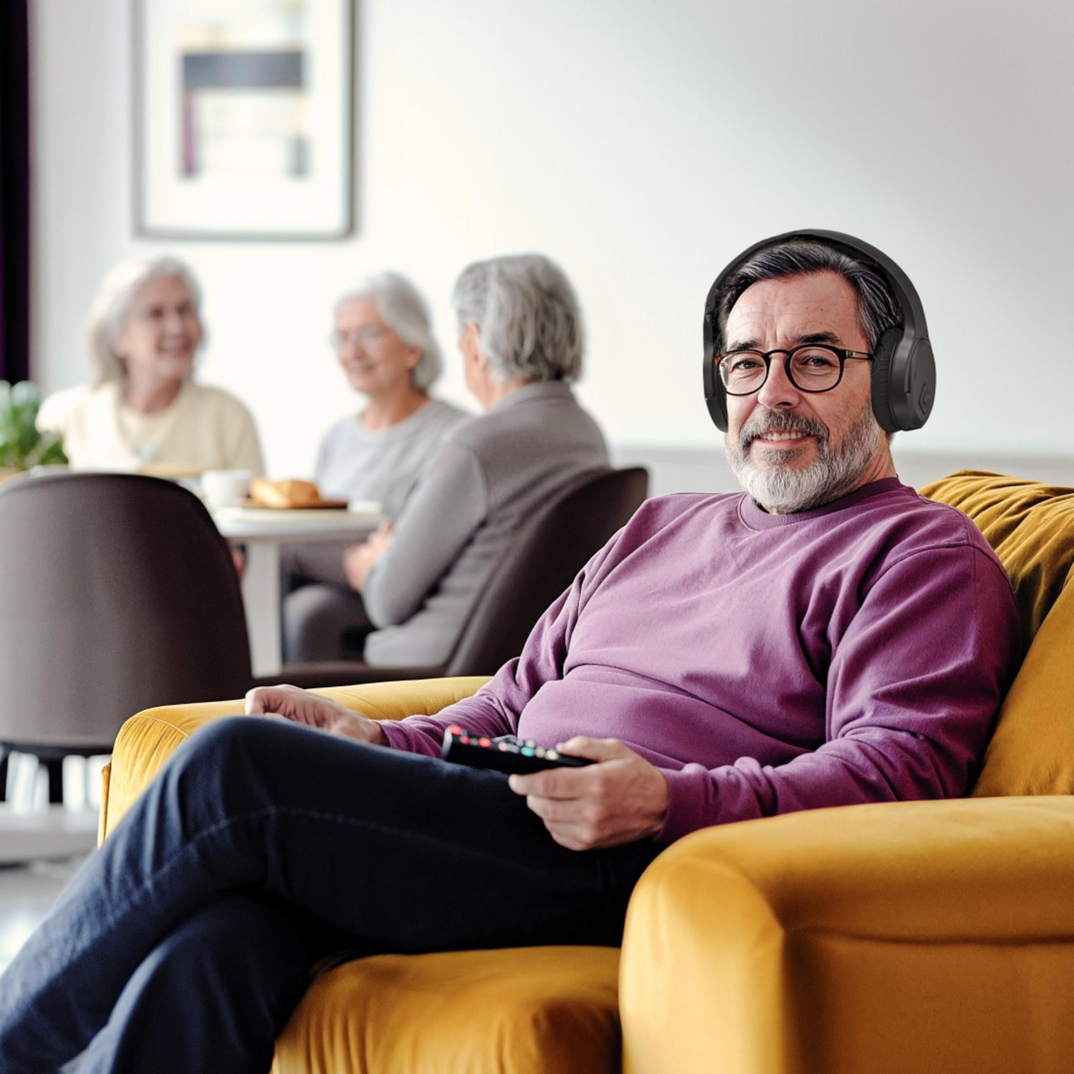 Ein Mann mit Kopfhörern sitzt auf einem gelben Sofa und hält eine Fernbedienung.