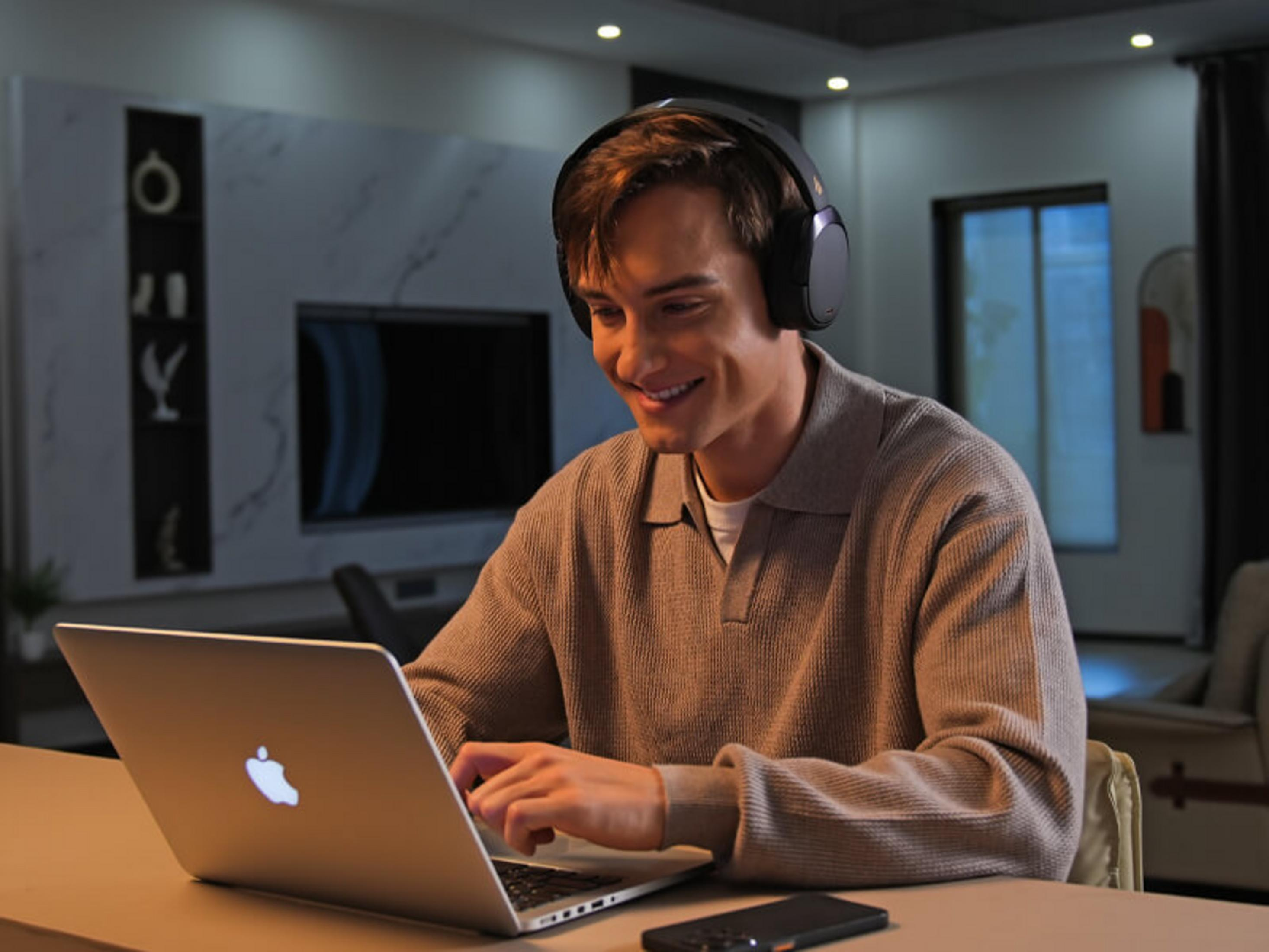 Mężczyzna w słuchawkach uśmiecha się, pisząc na laptopie.