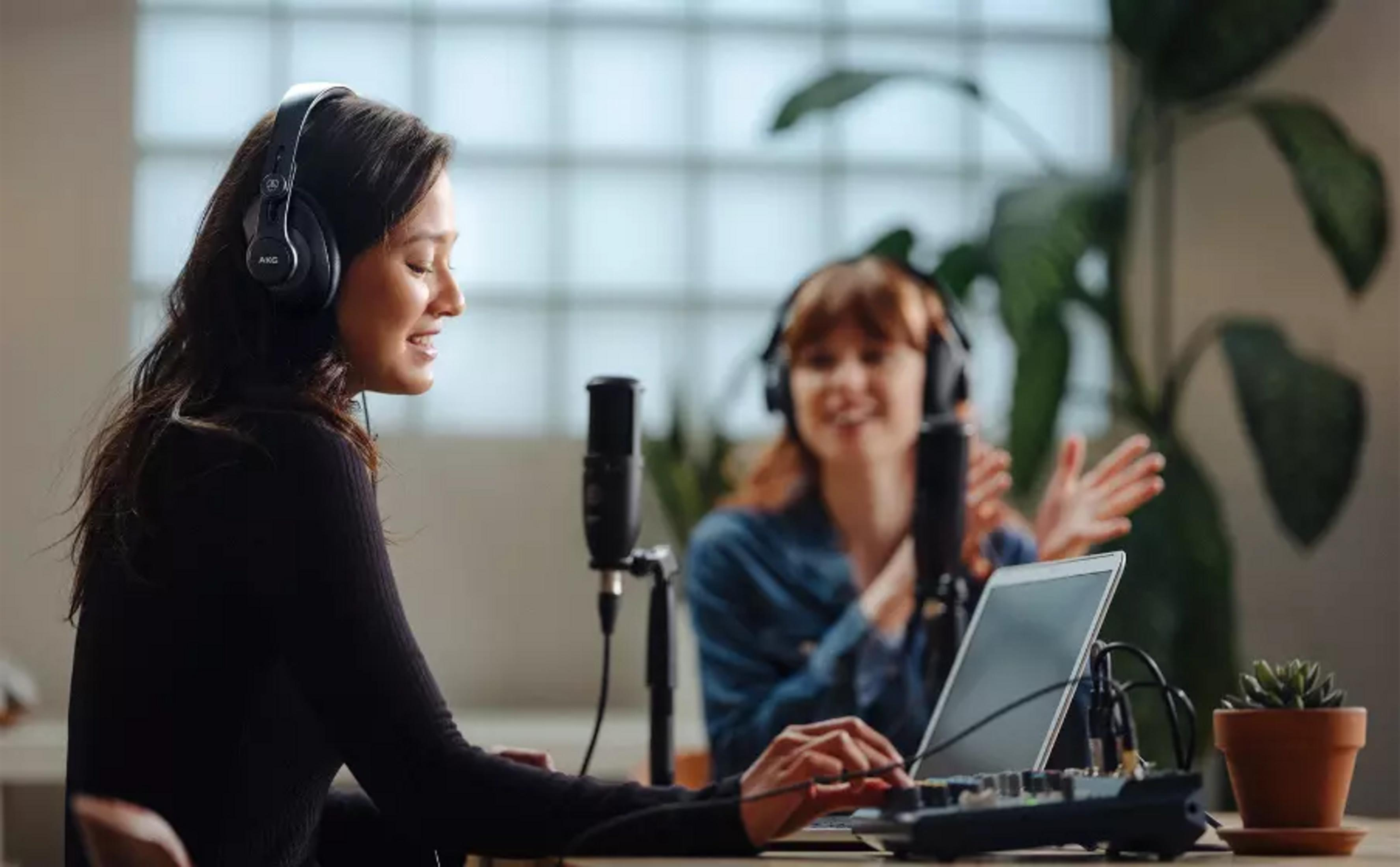 Zwei Frauen mit Kopfhörern in einem Aufnahmestudio, die Mikrofone und Mischpulte benutzen.