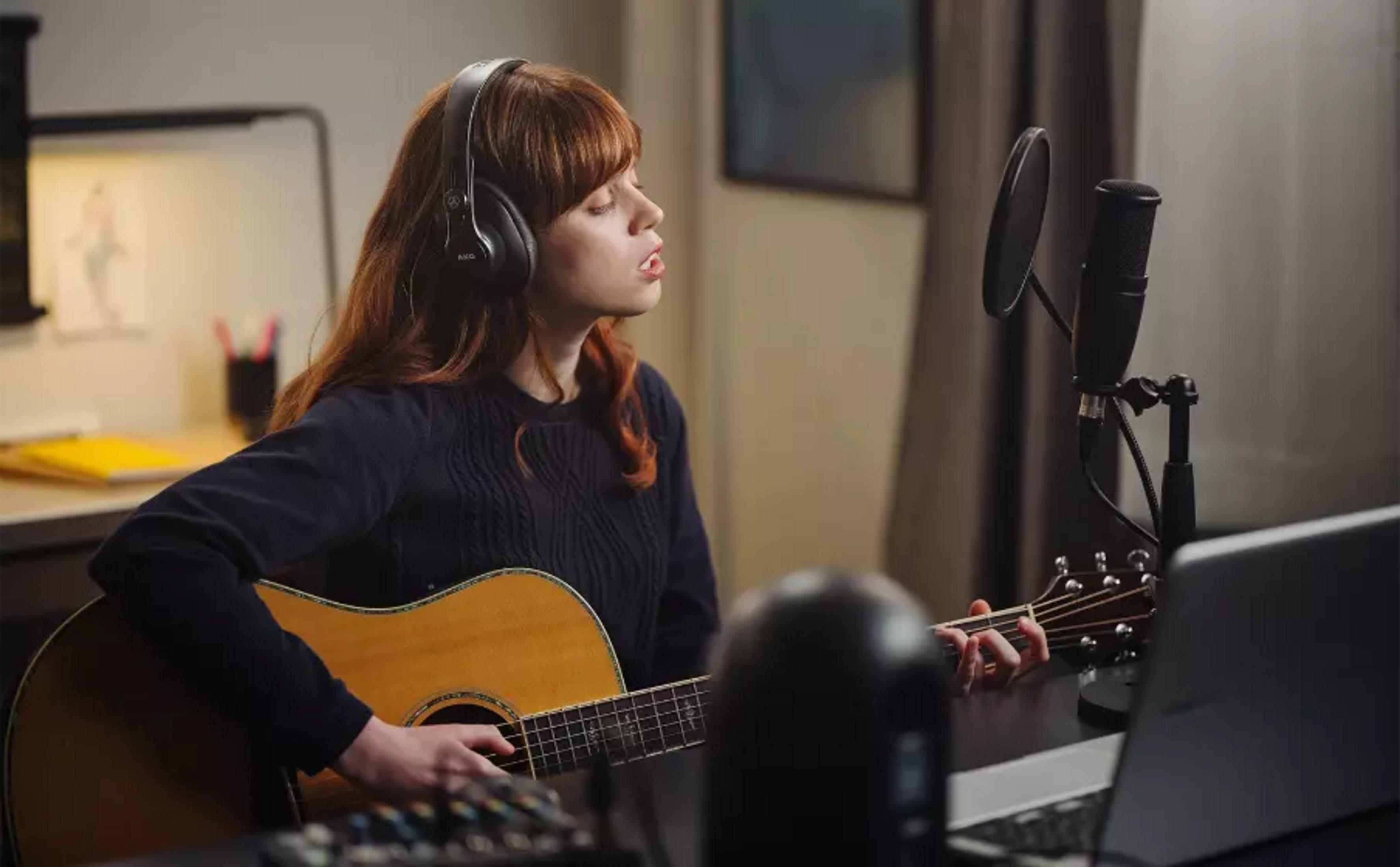 Una mujer con auriculares toca la guitarra y canta a un micrófono.