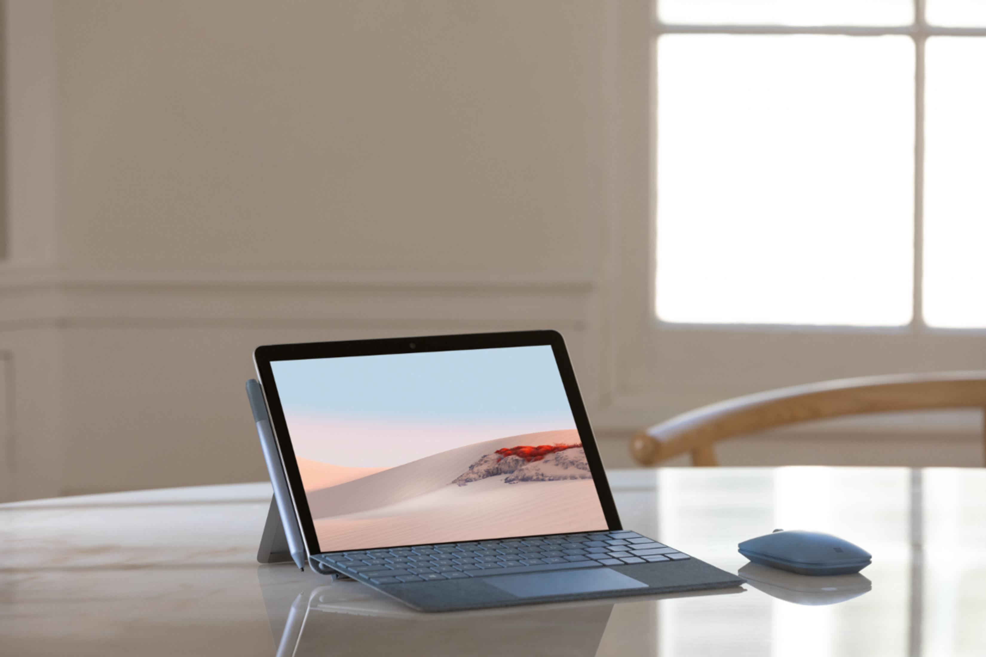 Ein graues Surface Laptop mit Stift und Maus auf einem Tisch.