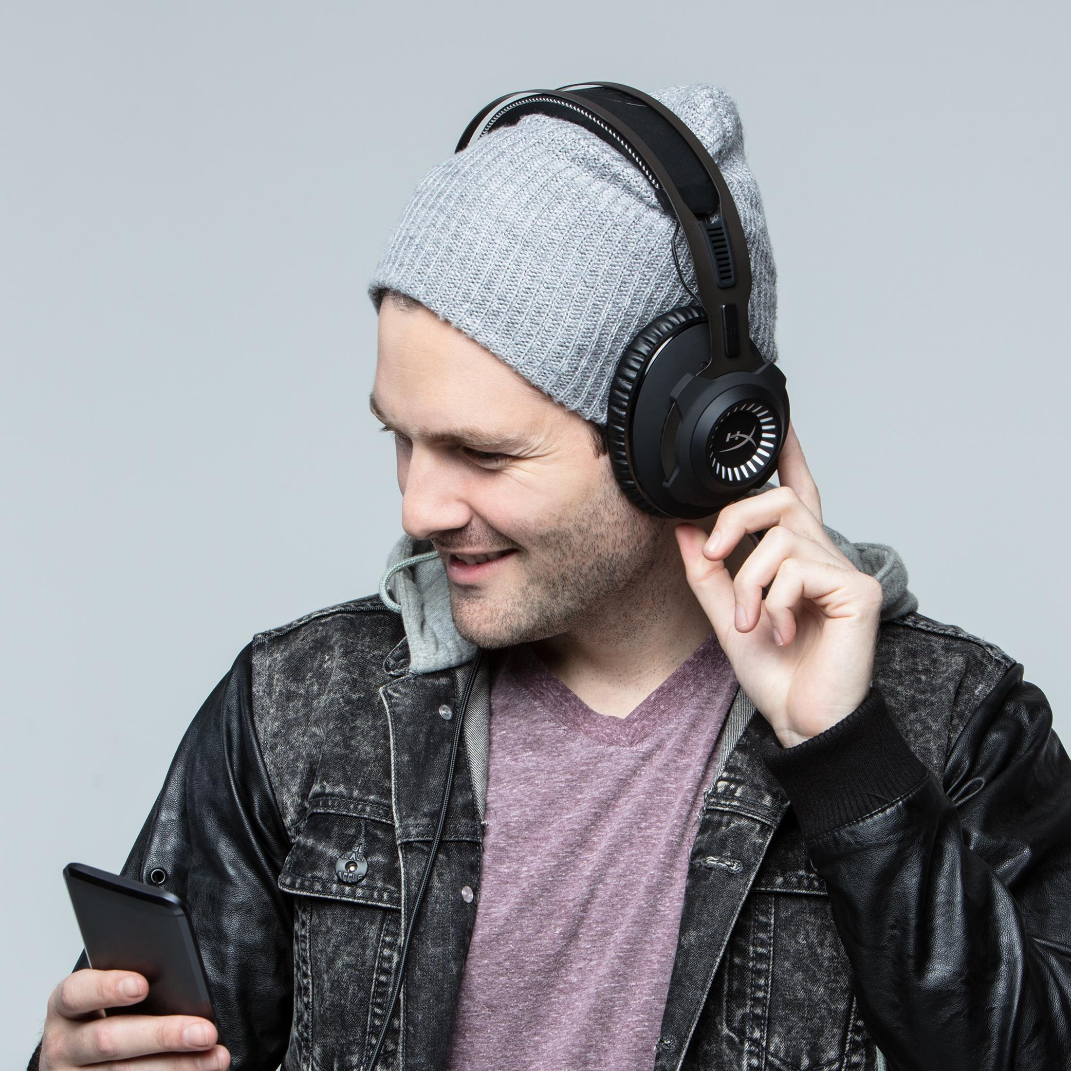 Ein Mann mit Kopfhörern und Beanie schaut auf sein Handy.