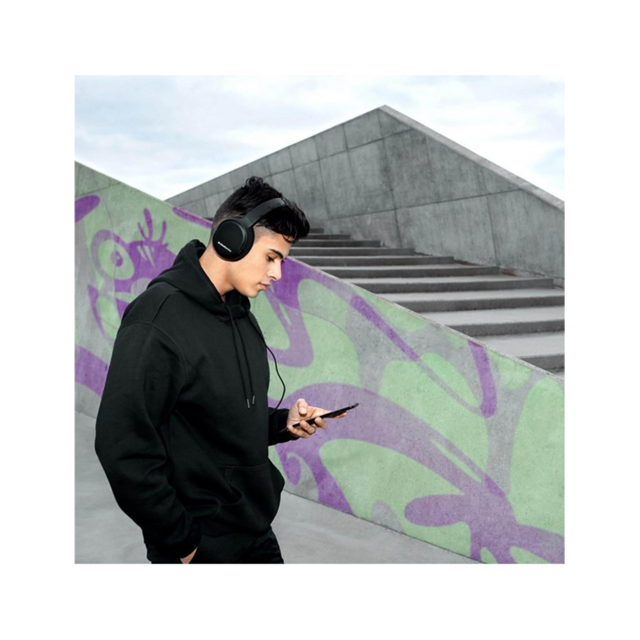 Ein Mann mit Kopfhörern schaut auf sein Handy vor einer Betonwand mit Graffiti.