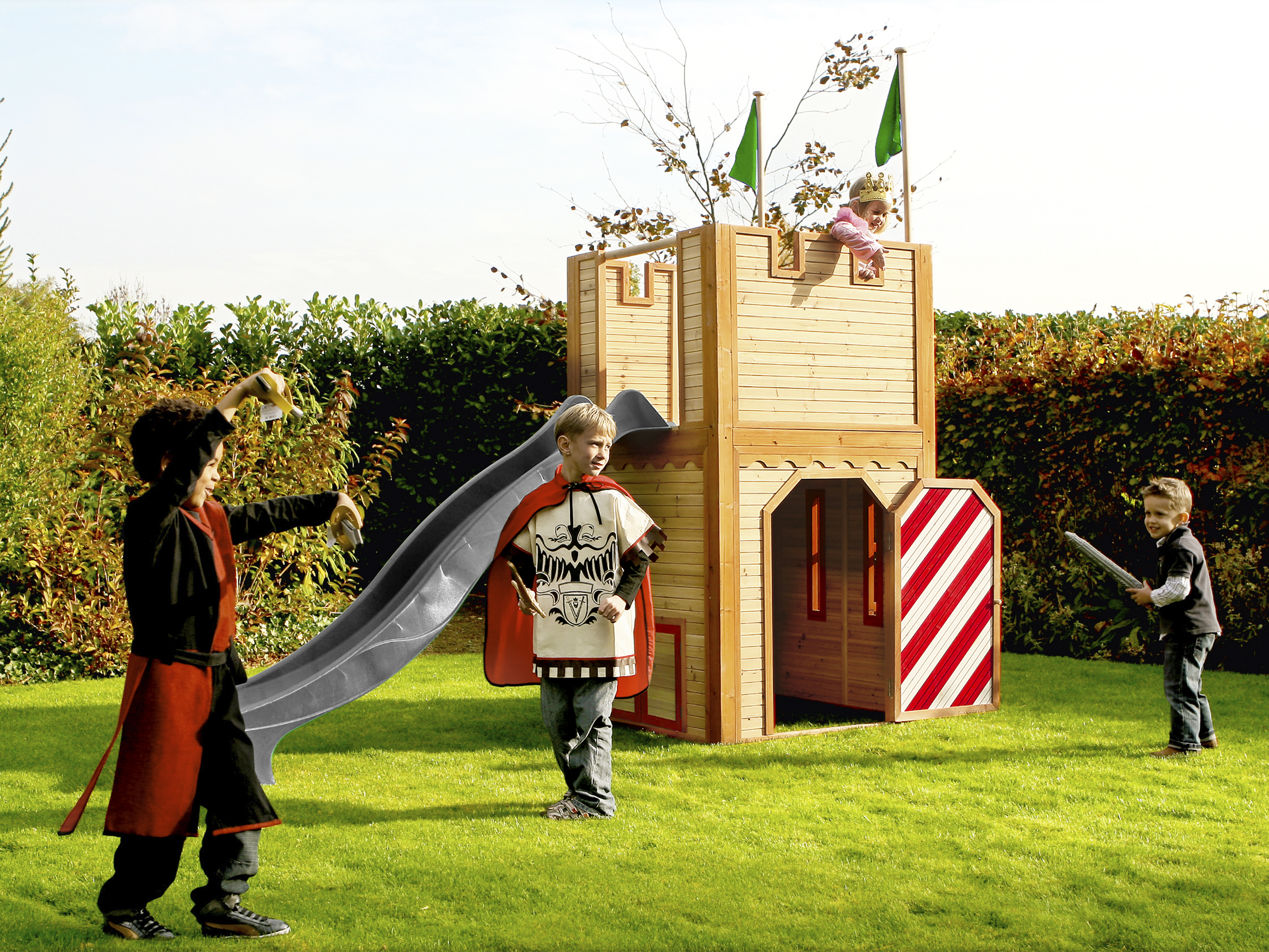 Kinder spielen Ritter vor einem Holzschloss mit Rutsche und Fahnen.