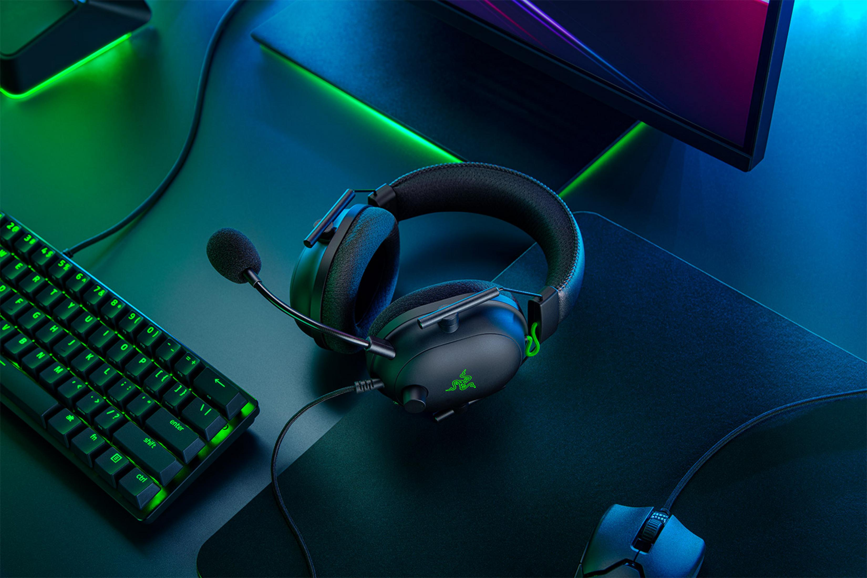 Auriculares negros para juegos con micrófono, teclado y ratón sobre un escritorio.