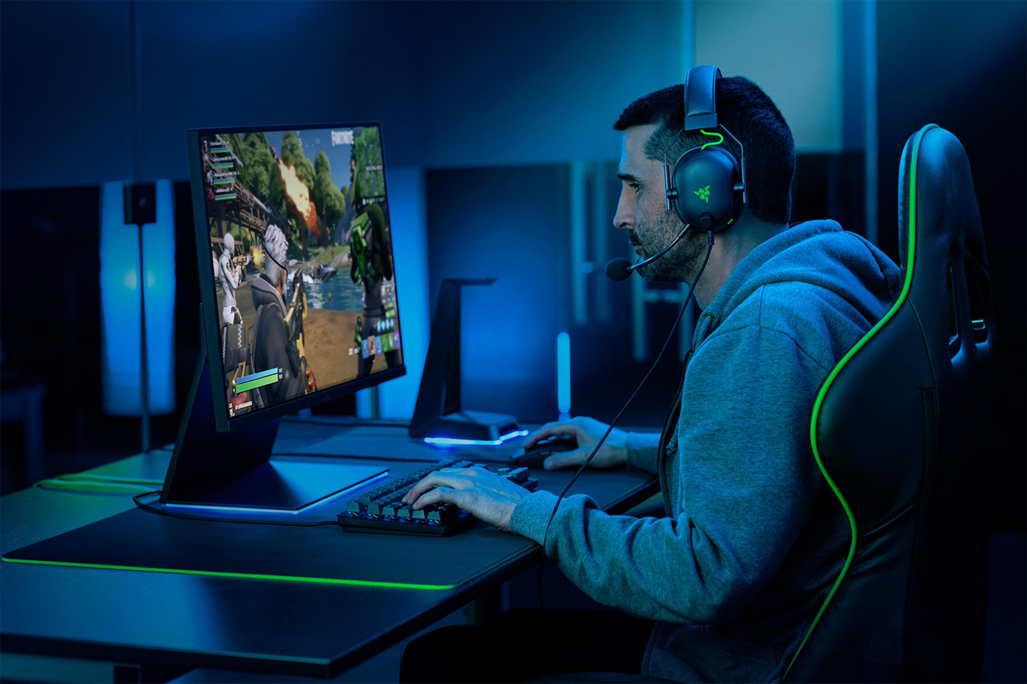Hombre con auriculares juega videojuego en computadora en sala oscura.