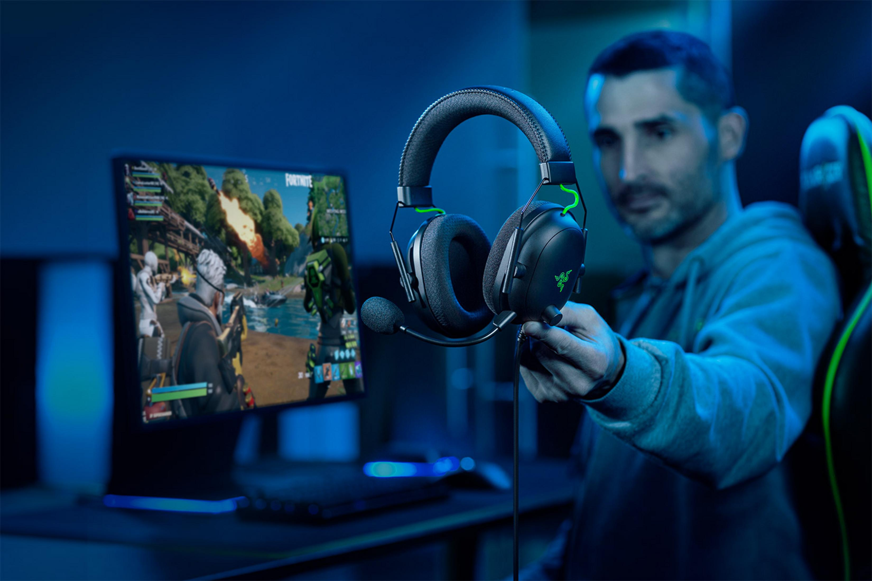 Hombre sostiene auriculares frente a una pantalla de PC gamer con Fortnite.