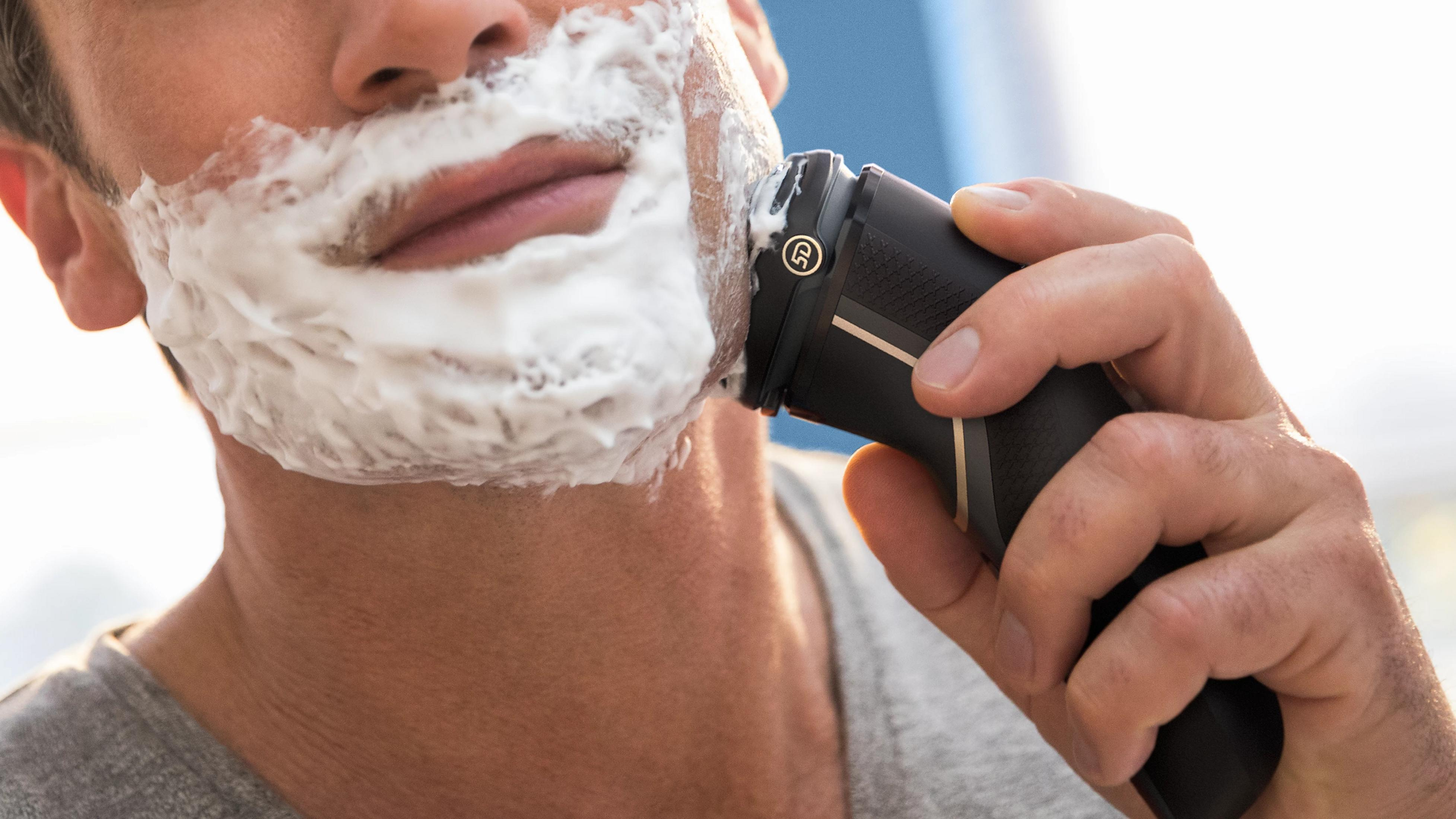 Man shaving his face with an electric razor and shaving foam.