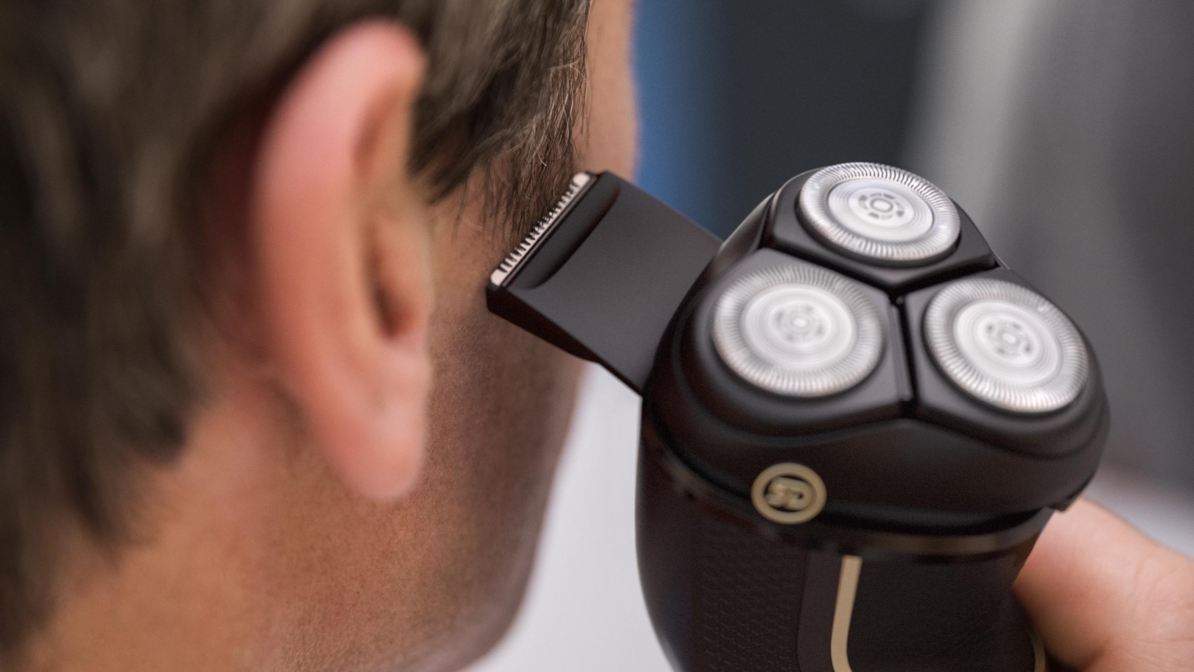 A man shaves the hair on his neck with an electric shaver.