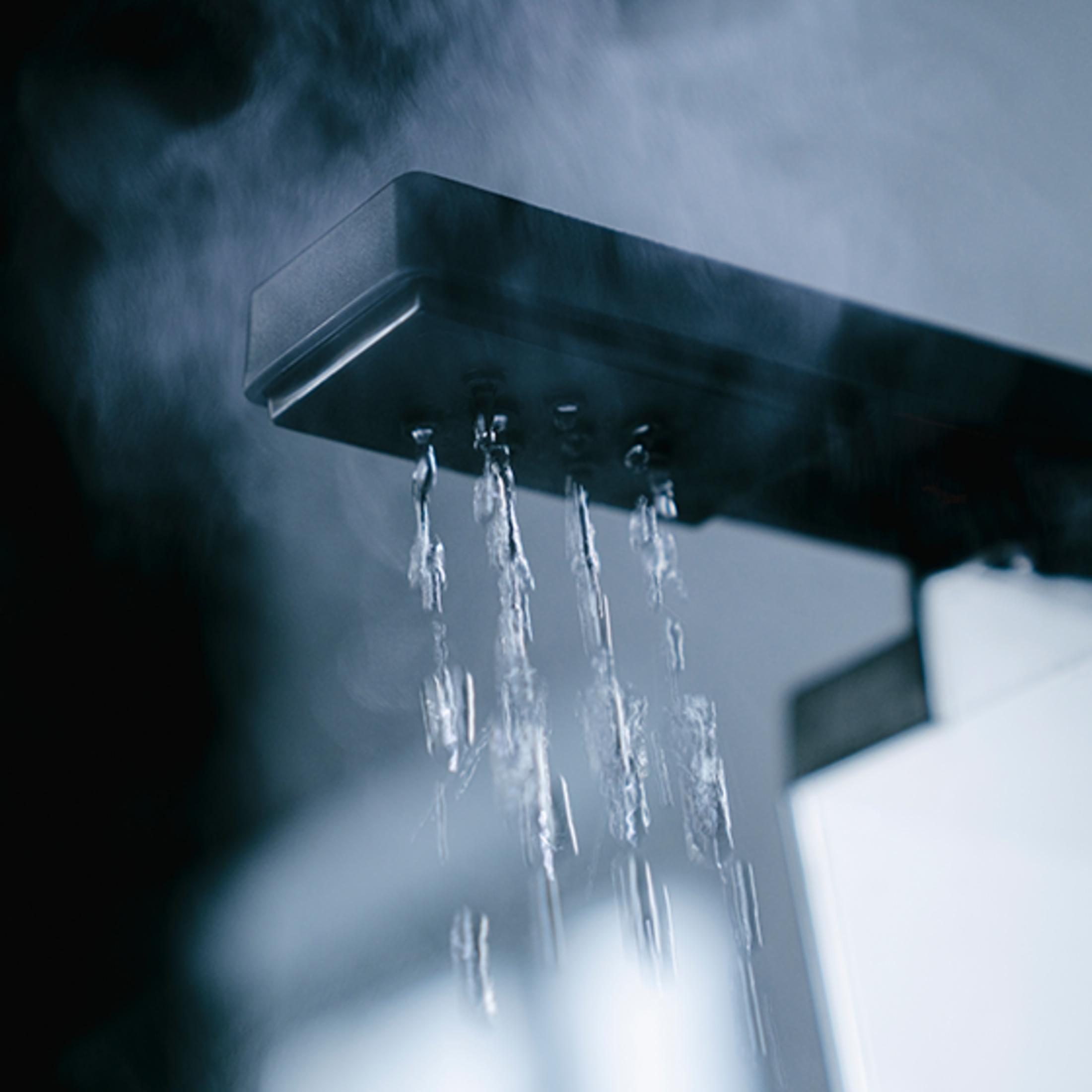 Strumienie wody lecą z nowoczesnej głowicy prysznicowej, unosi się para.