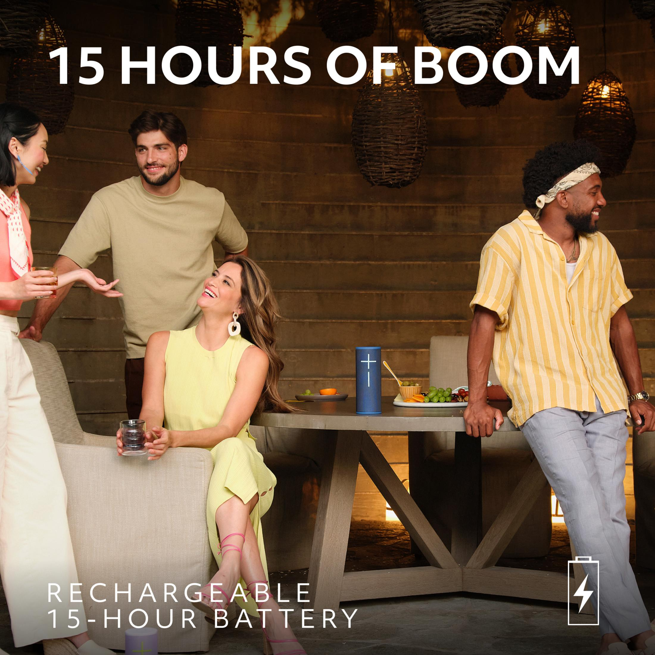 Czterech przyjaciół siedzi przy stoliku na zewnątrz z niebieskim głośnikiem.