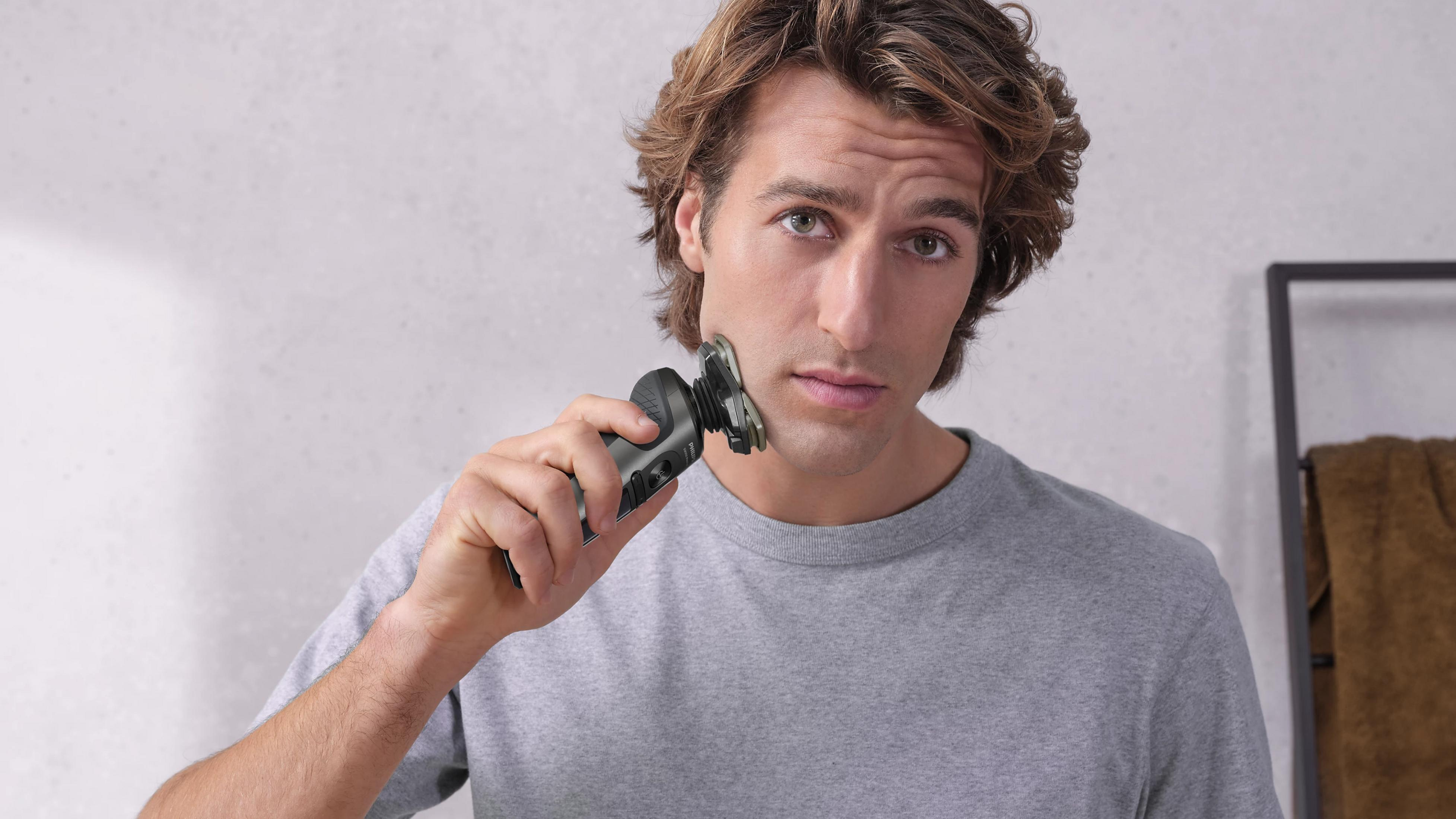 Un hombre con pelo castaño se afeita la cara con una afeitadora eléctrica negra.