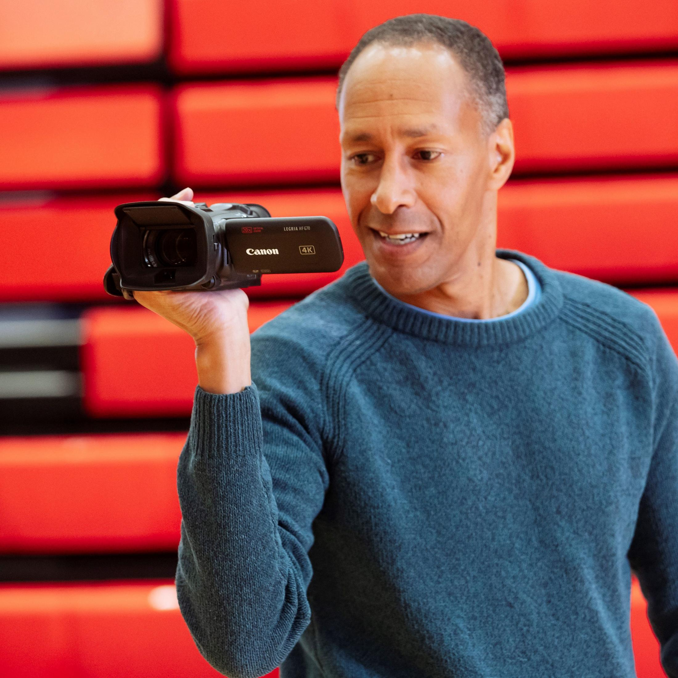 Un hombre con suéter azul sostiene una videocámara Canon 4K.