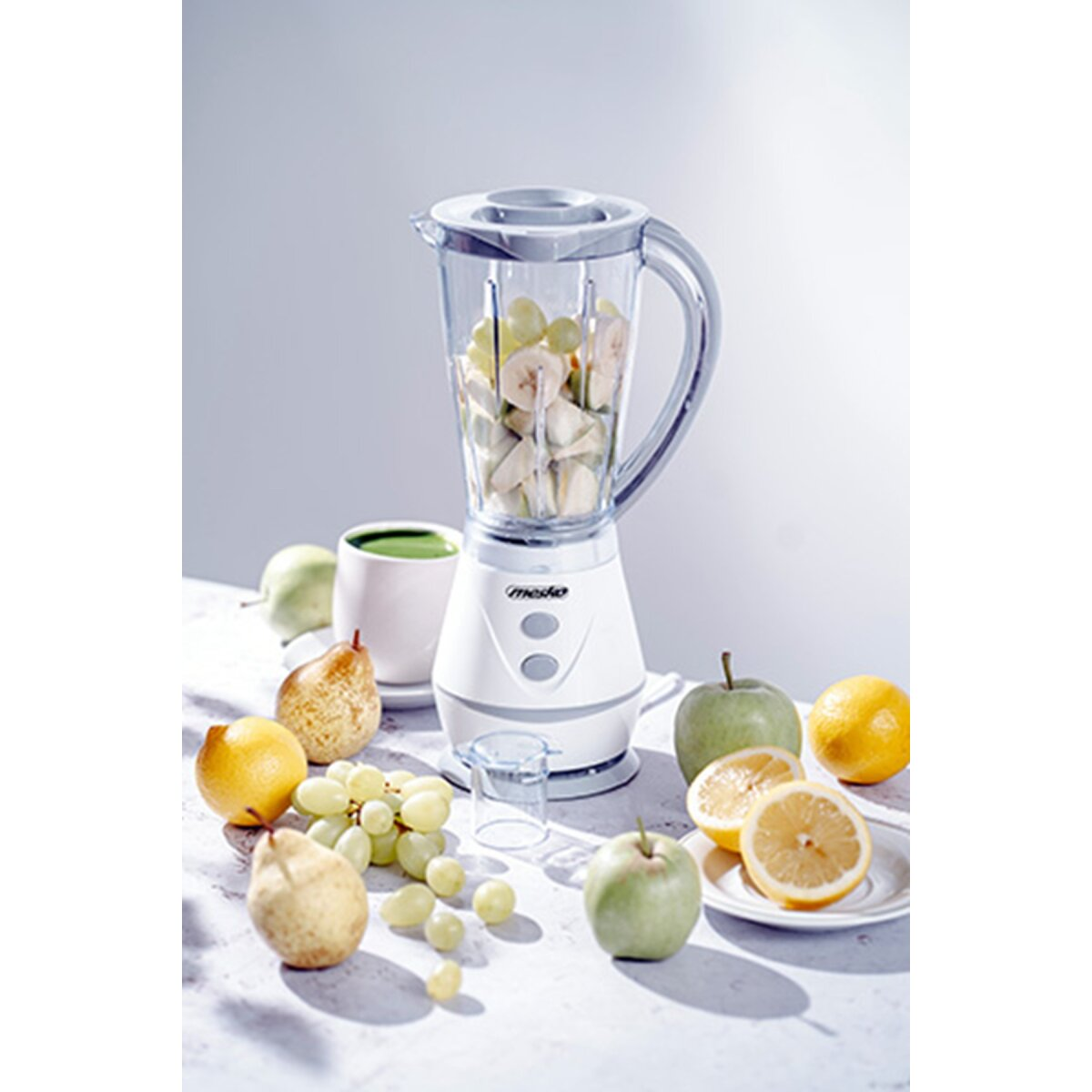 Ein Mixer mit Früchten wie Trauben, Bananen, Äpfeln und Zitronen.