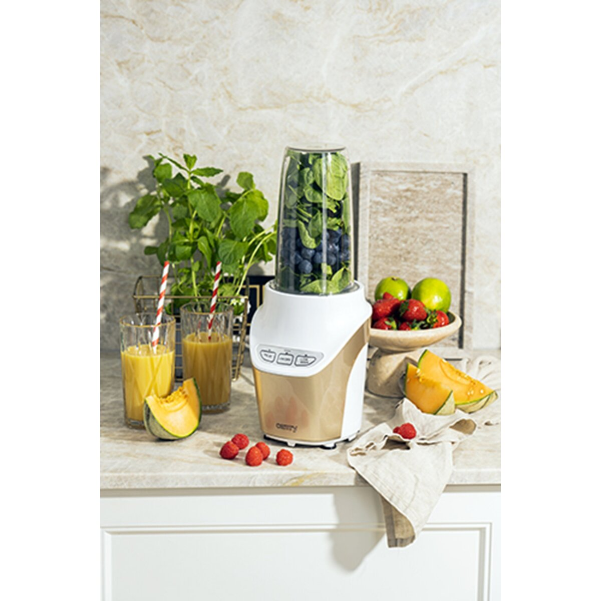 Una licuadora con arándanos y espinacas, fruta y jugo al lado.