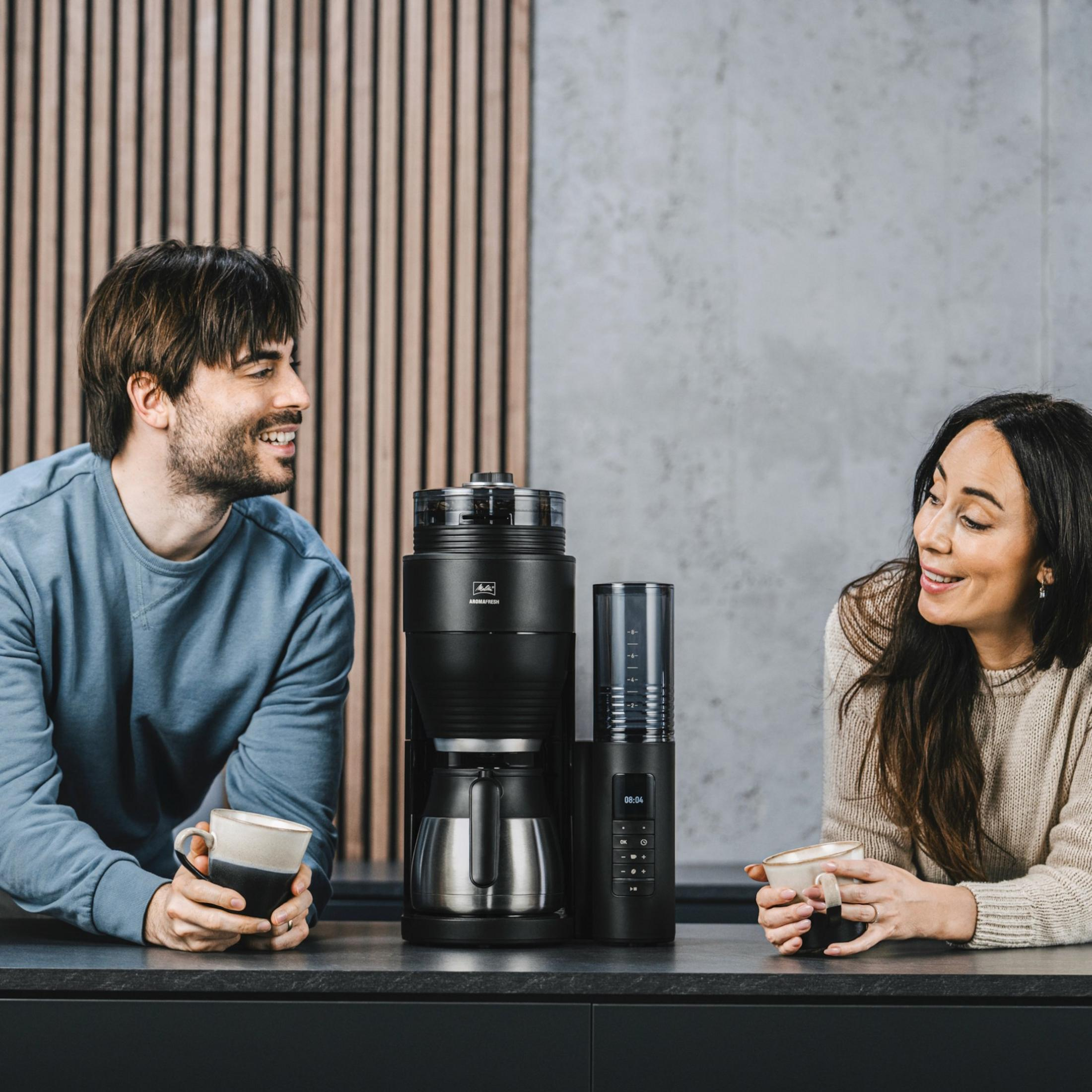 Mężczyzna i kobieta piją kawę obok ekspresu do kawy.