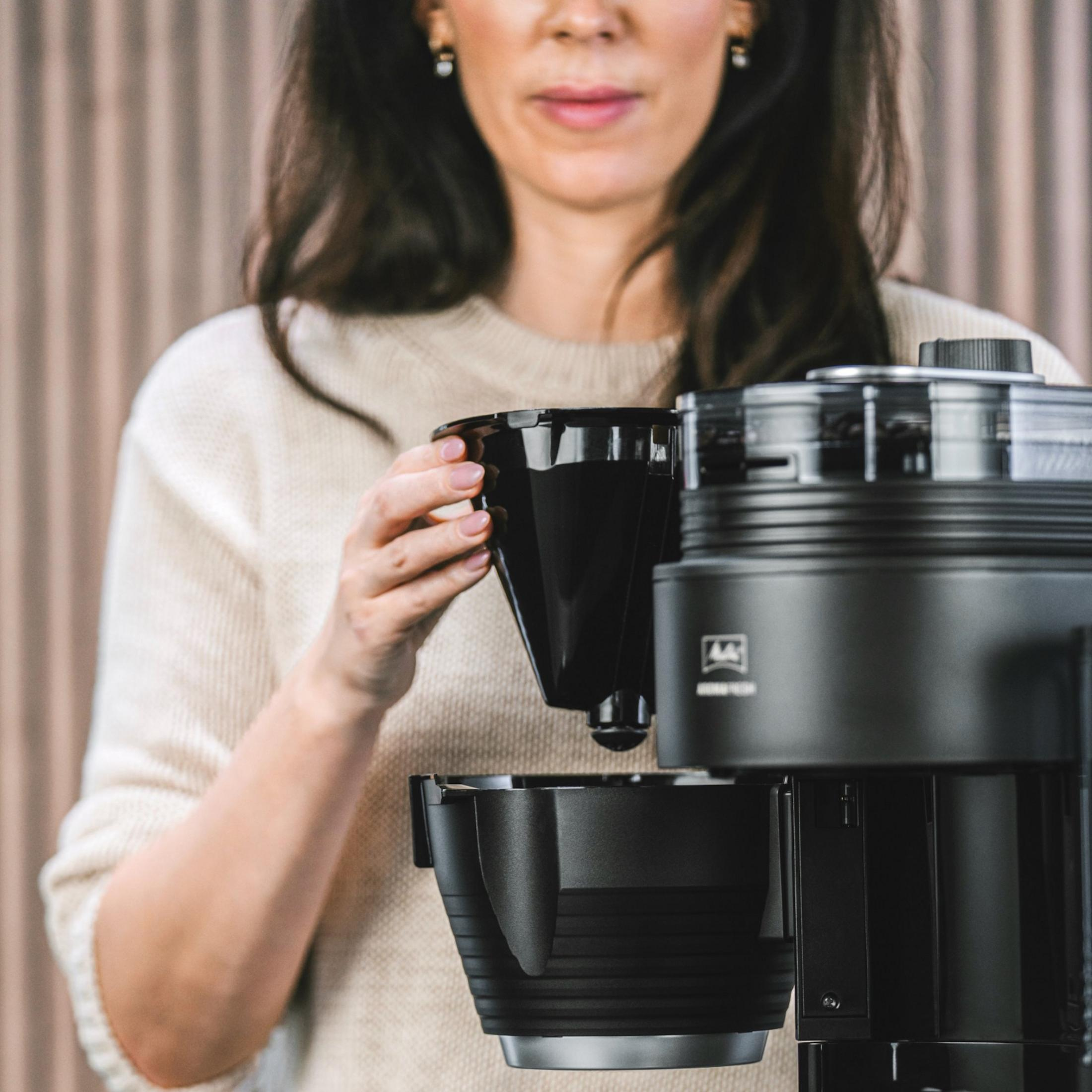 Kobieta w beżowym swetrze wkłada czarny filtr do kawy do ekspresu do kawy.